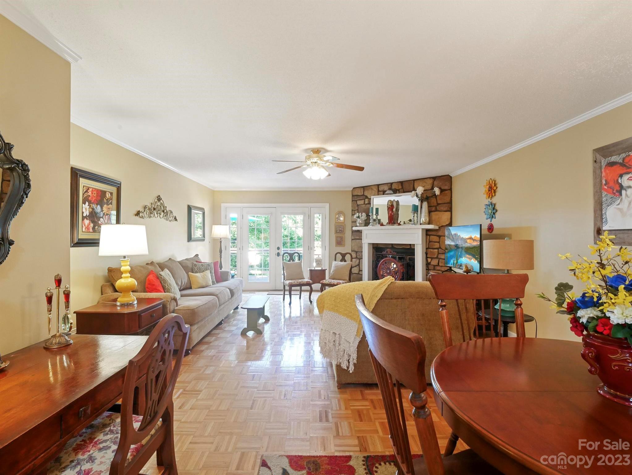 Furnished living and dining room with parquet flooring, a stone fireplace, and French doors.
