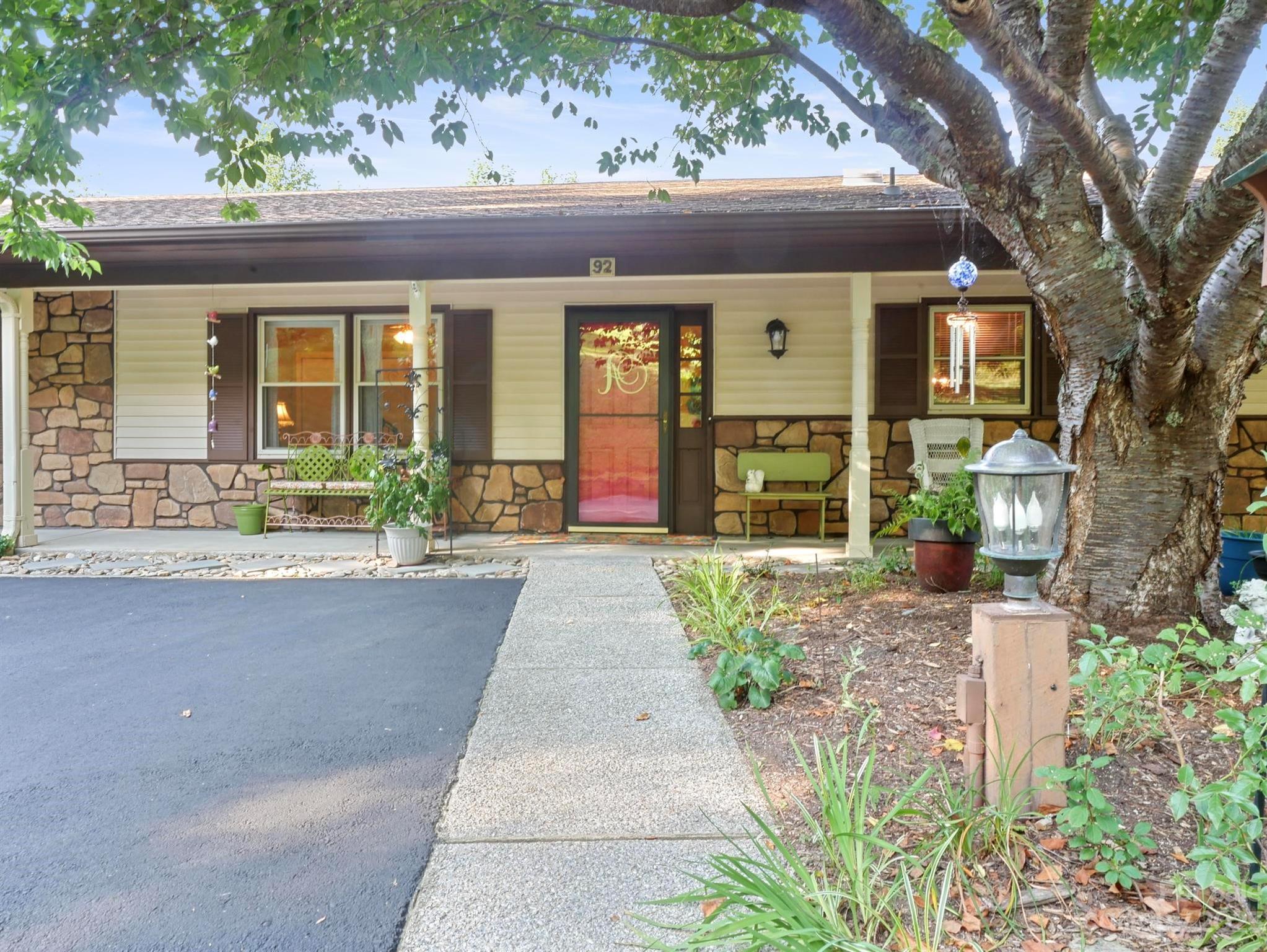 Home front with stone facade, red entry door, and a large shade tree beside the walkway.