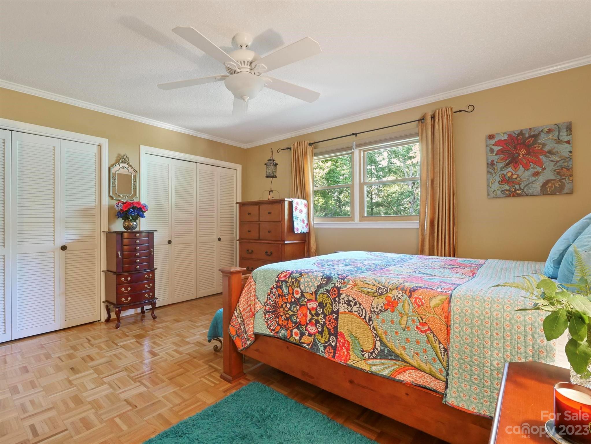 Bedroom with a colorful patchwork quilt, parquet flooring, and white louvered closets.