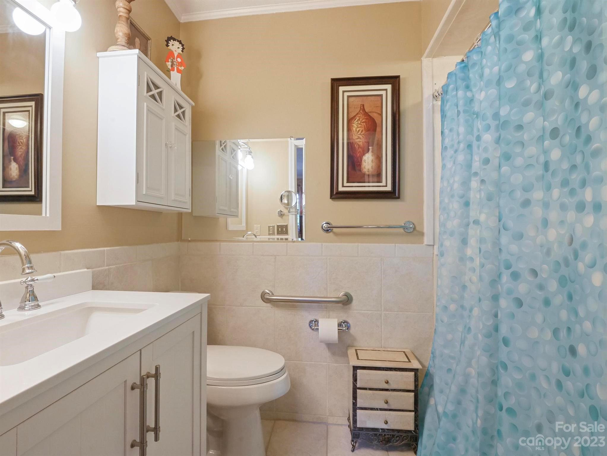 Bathroom with a white vanity, tiled walls, grab bars, and a blue patterned shower curtain.