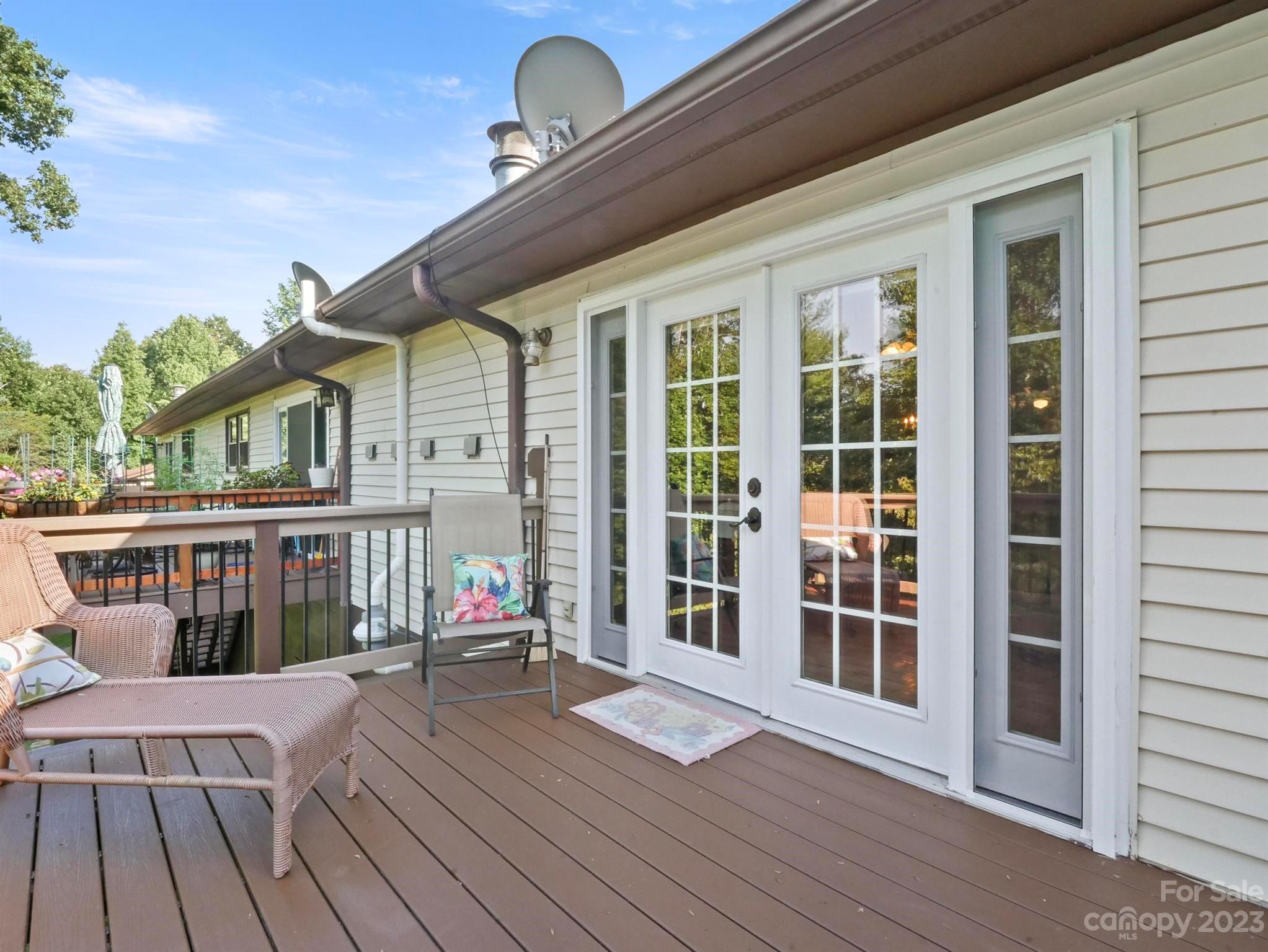 Deck with wicker seating beside white French doors on a light-sided home.