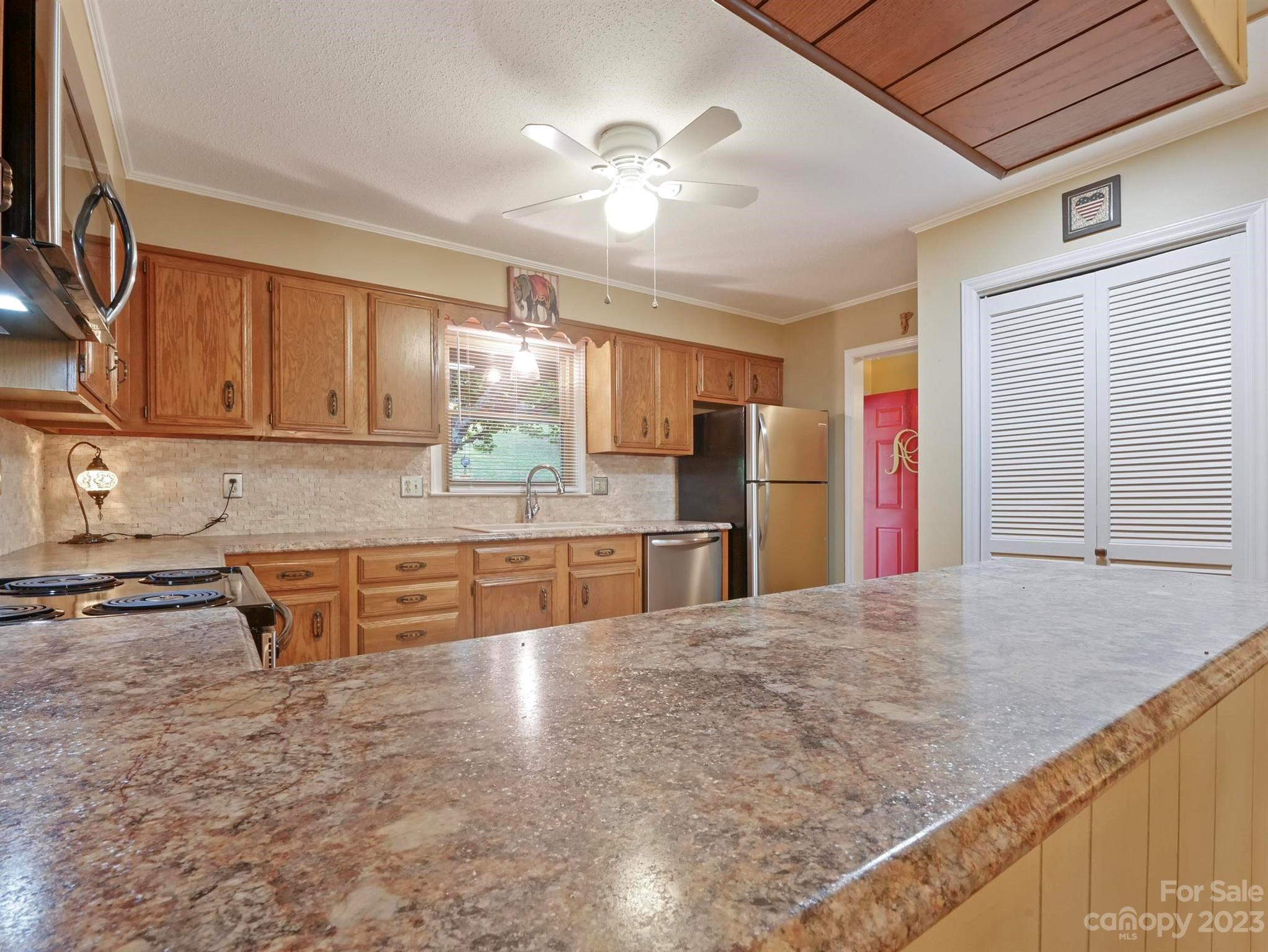 Kitchen with wood cabinets, a large stone countertop peninsula, and stainless steel appliances.
