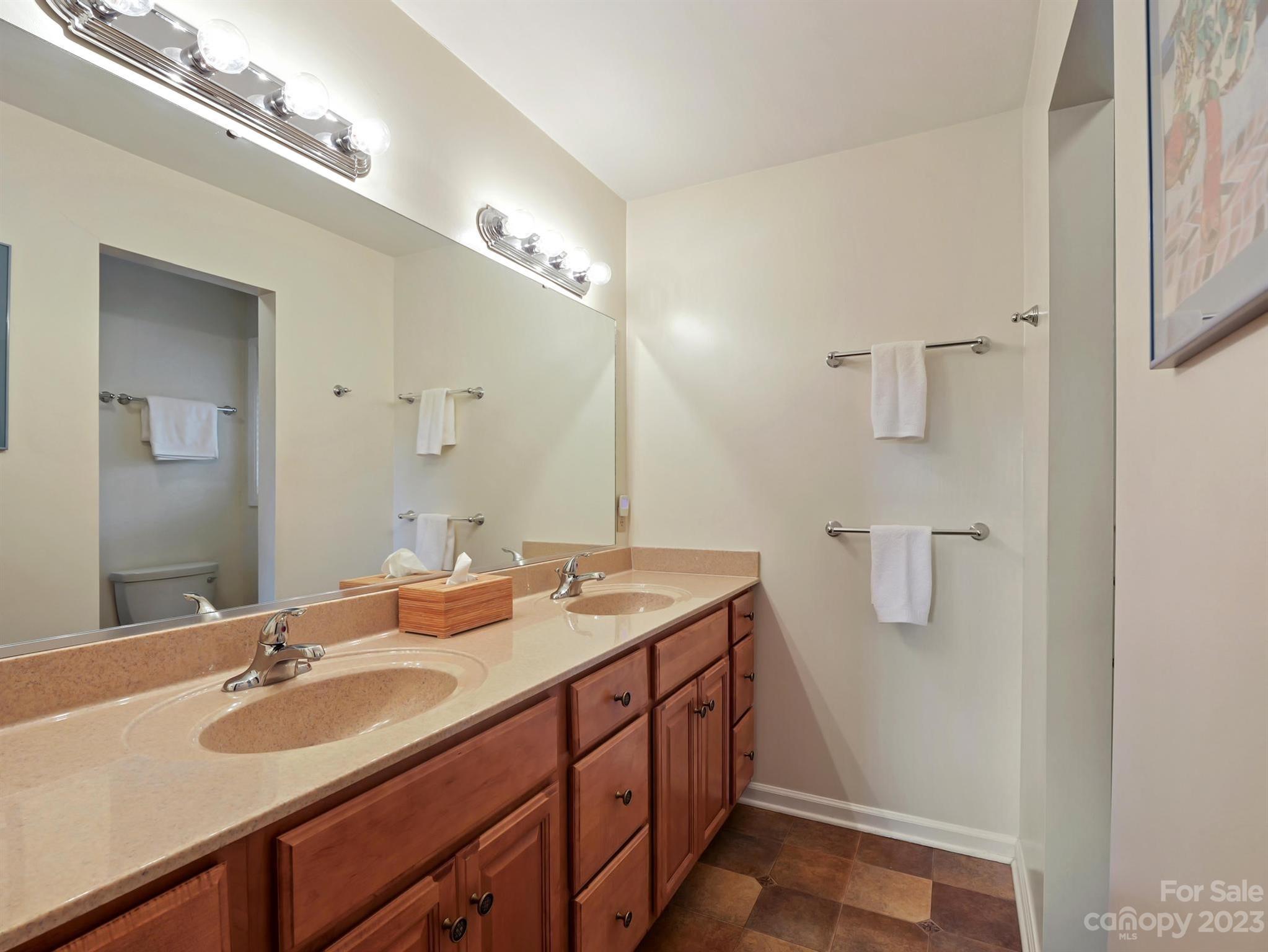 Bathroom with a double-sink vanity, warm wood cabinets, and a large mirror.