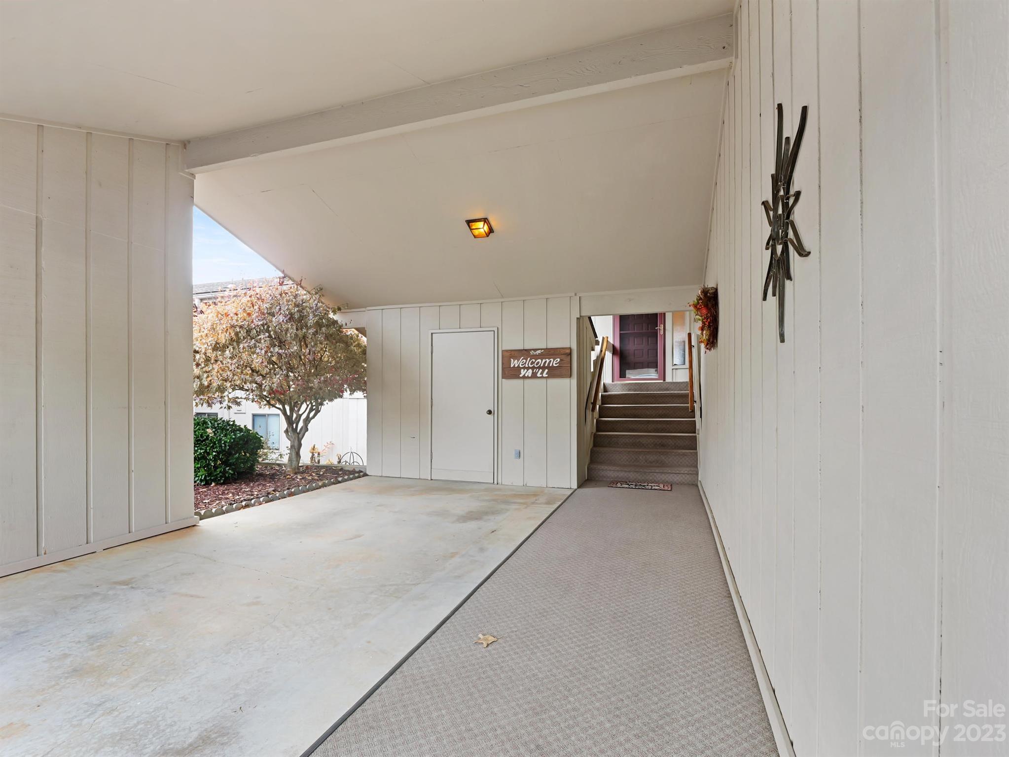 Covered entrance with a concrete carport, carpeted walkway, and stairs leading to the front door.