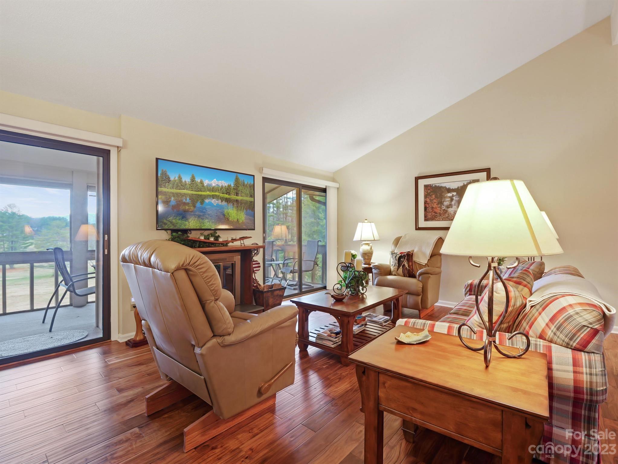 Furnished living room with hardwood floors, recliners, plaid seating, and sliding doors to a balcony.