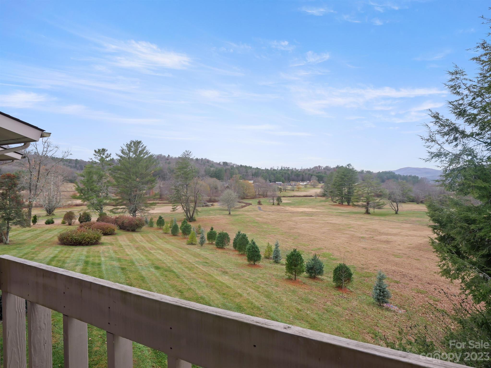Panoramic lawn and wooded hills viewed over a wooden deck railing, with distant mountains on the horizon.