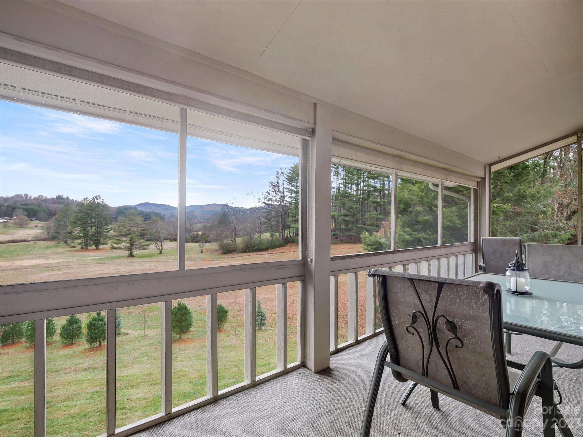 Screened porch with a dining set overlooking a grassy yard, trees, and distant mountains.