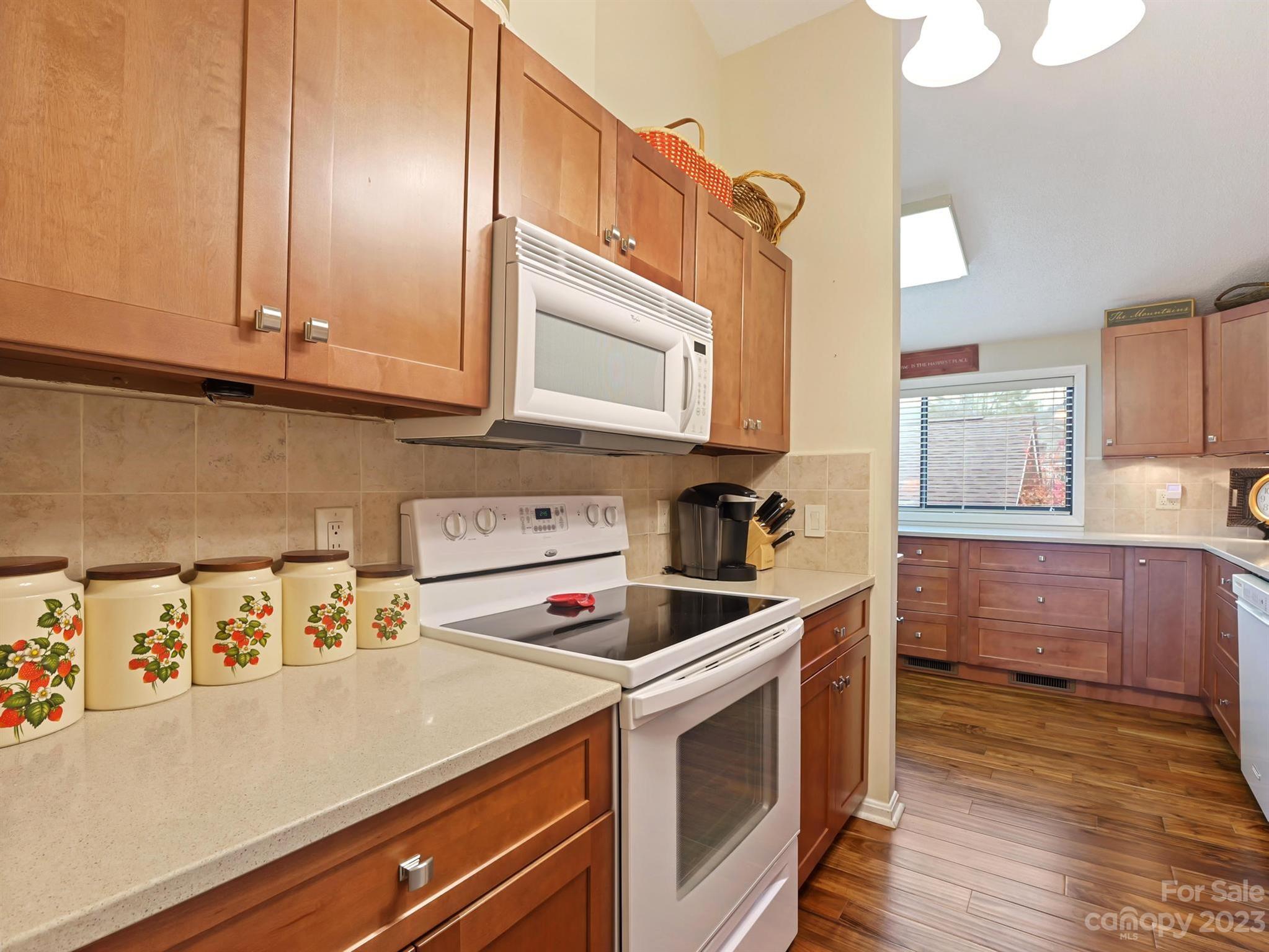 Kitchen with warm wood cabinetry, white appliances, strawberry-patterned canisters, and wood-look flooring.