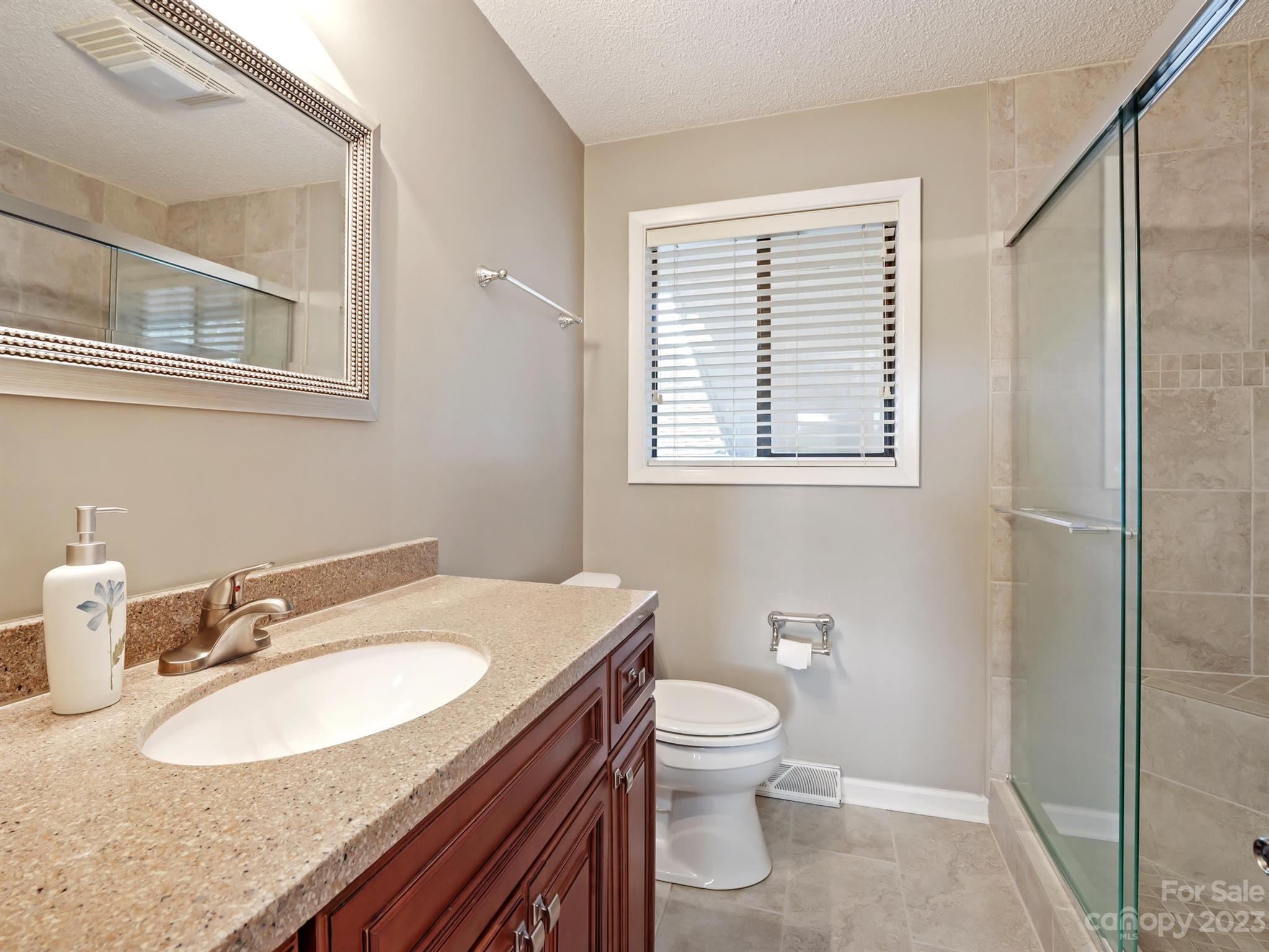 Bathroom with a granite-look vanity, dark wood cabinets, and a glass-enclosed tiled shower.