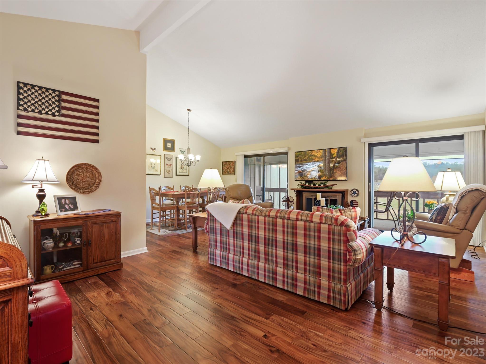 Furnished living room with vaulted ceiling, hardwood floors, plaid sofa, and sliding doors to a balcony.