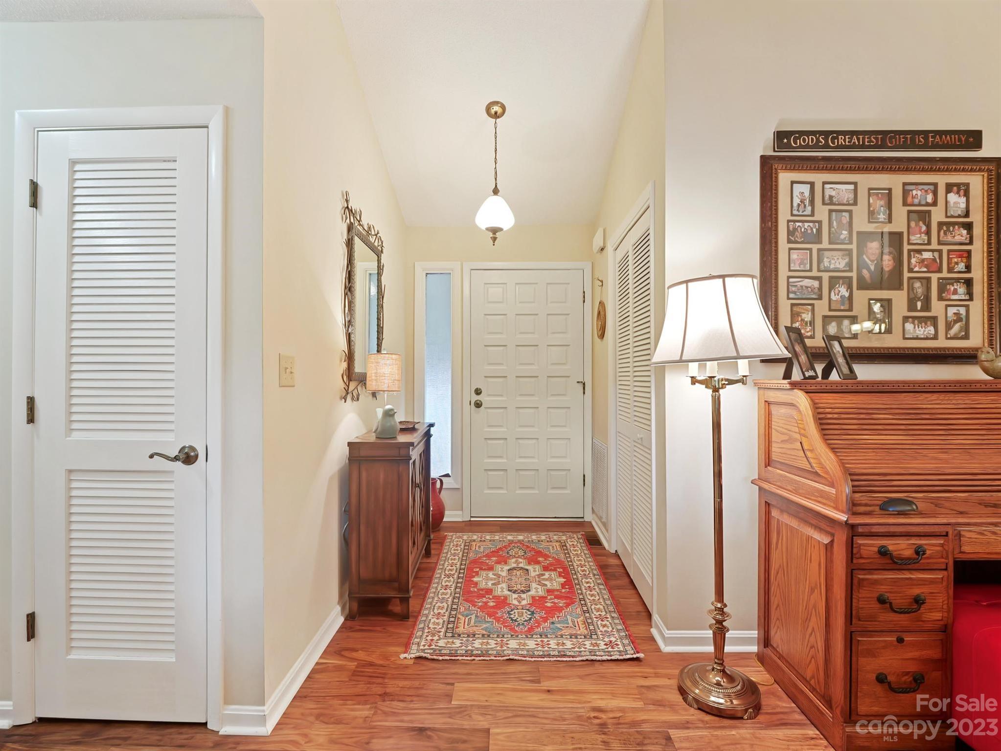 Furnished entryway with hardwood floors, a patterned runner, and a wooden cabinet topped by family photos.