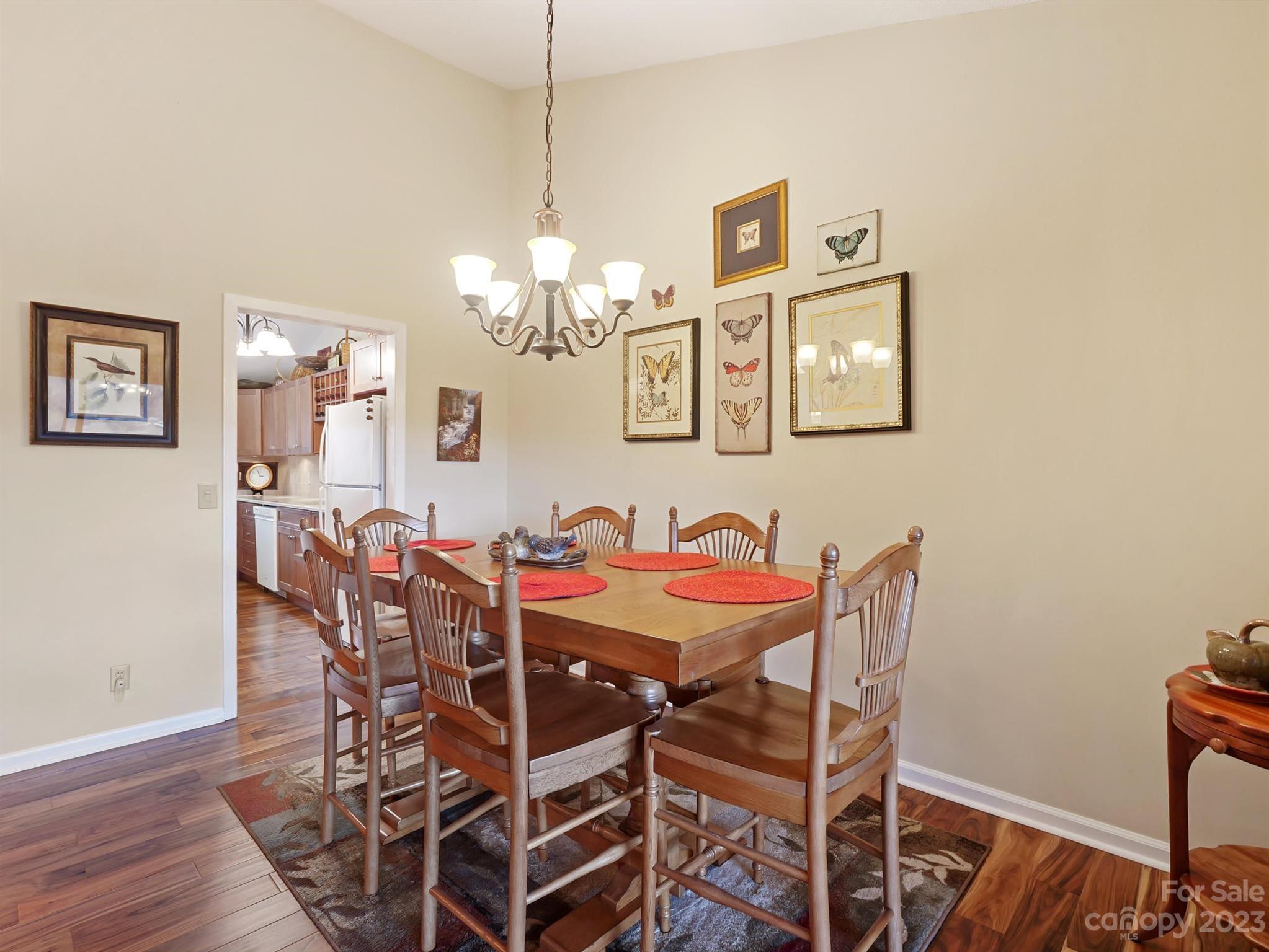 Dining room with a wooden table, spindle-back chairs, chandelier, and framed butterfly art.