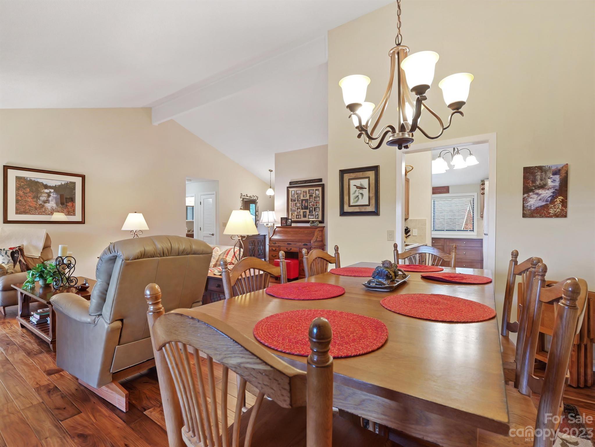 Dining area with a wooden table, red placemats, chandelier, and adjoining living room.