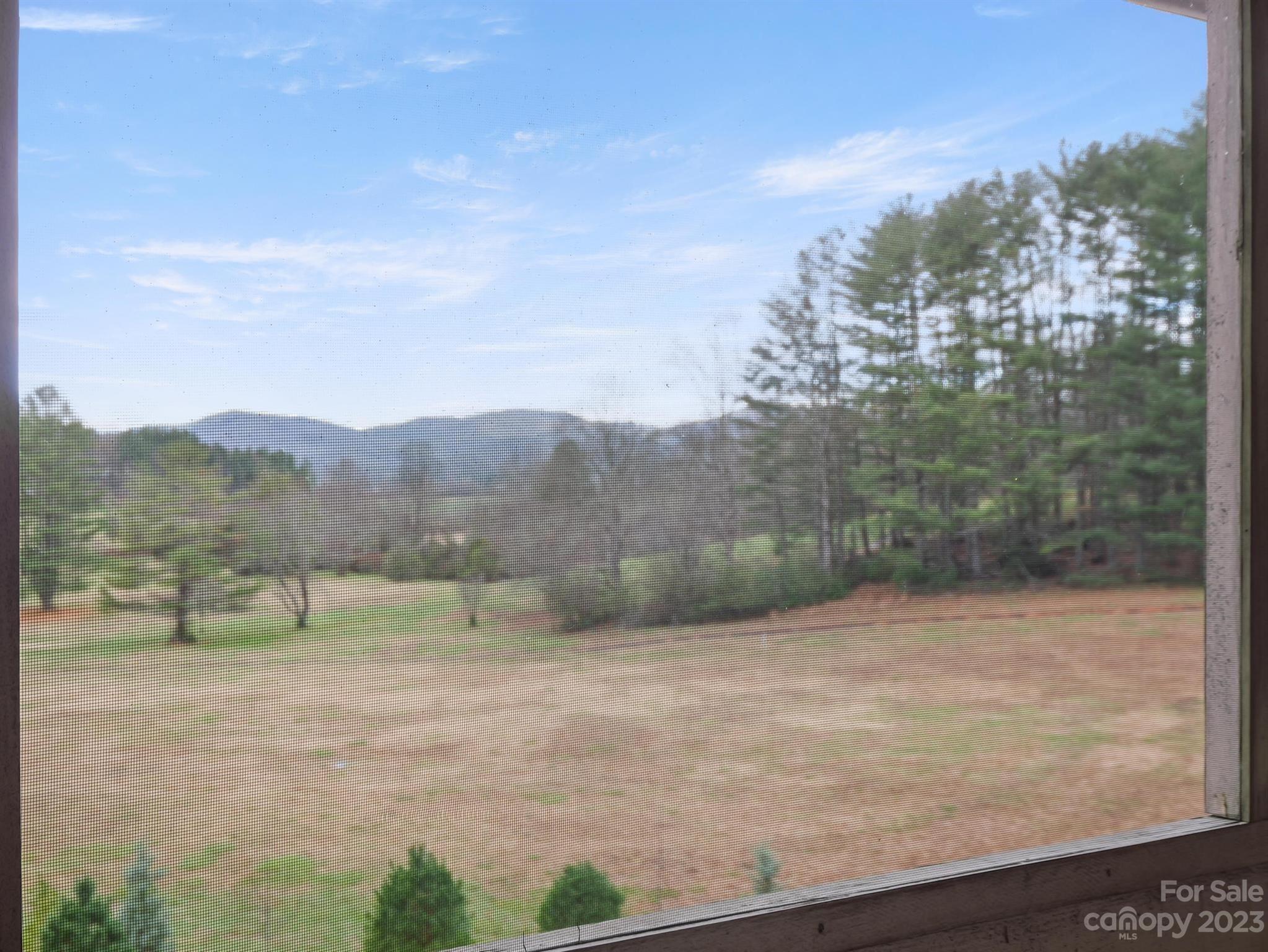 Mountain view through a screened window, overlooking a broad lawn and wooded ridgelines.