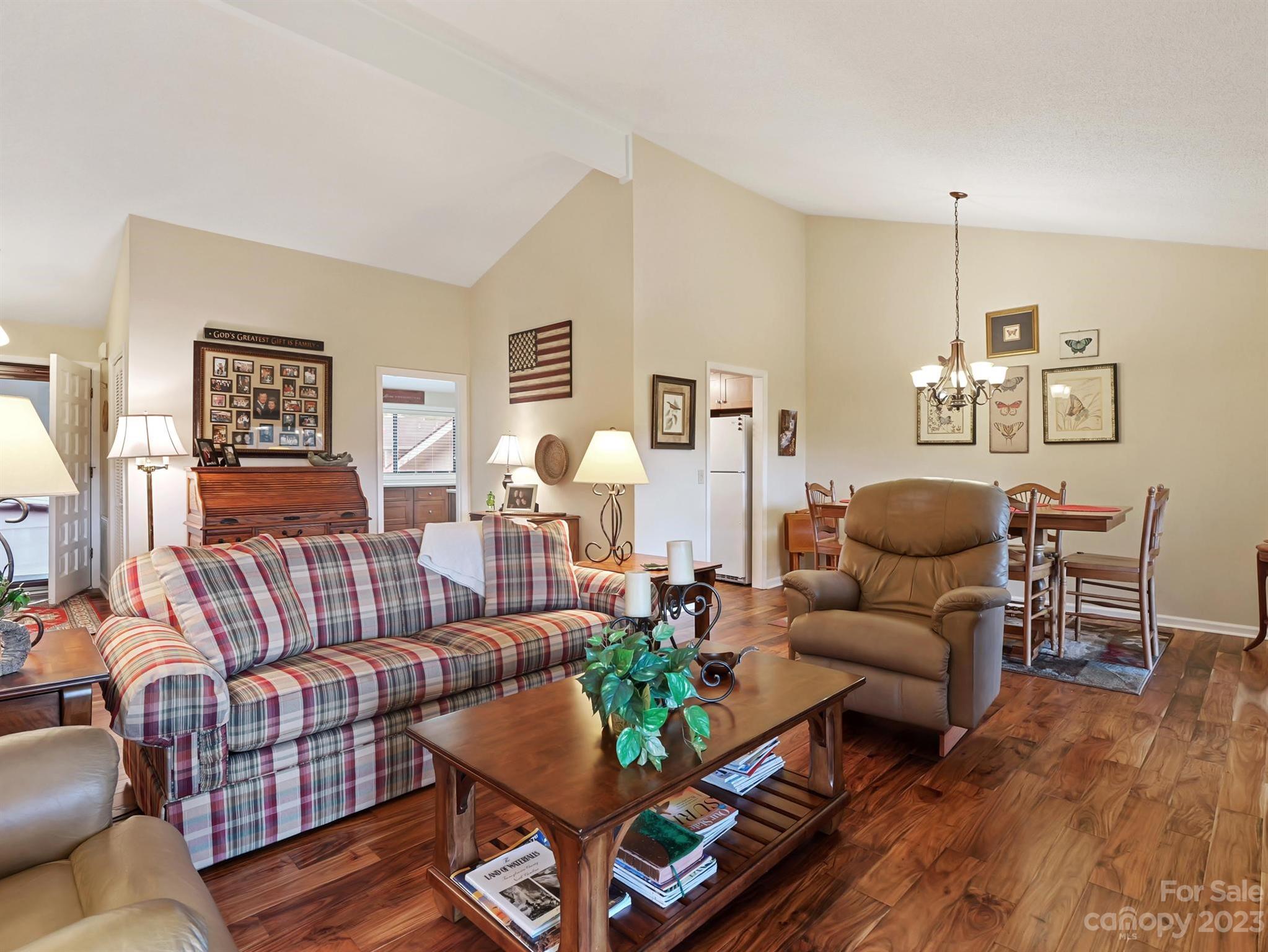 Living room with a plaid sofa, leather recliner, vaulted ceiling, and adjoining dining area.