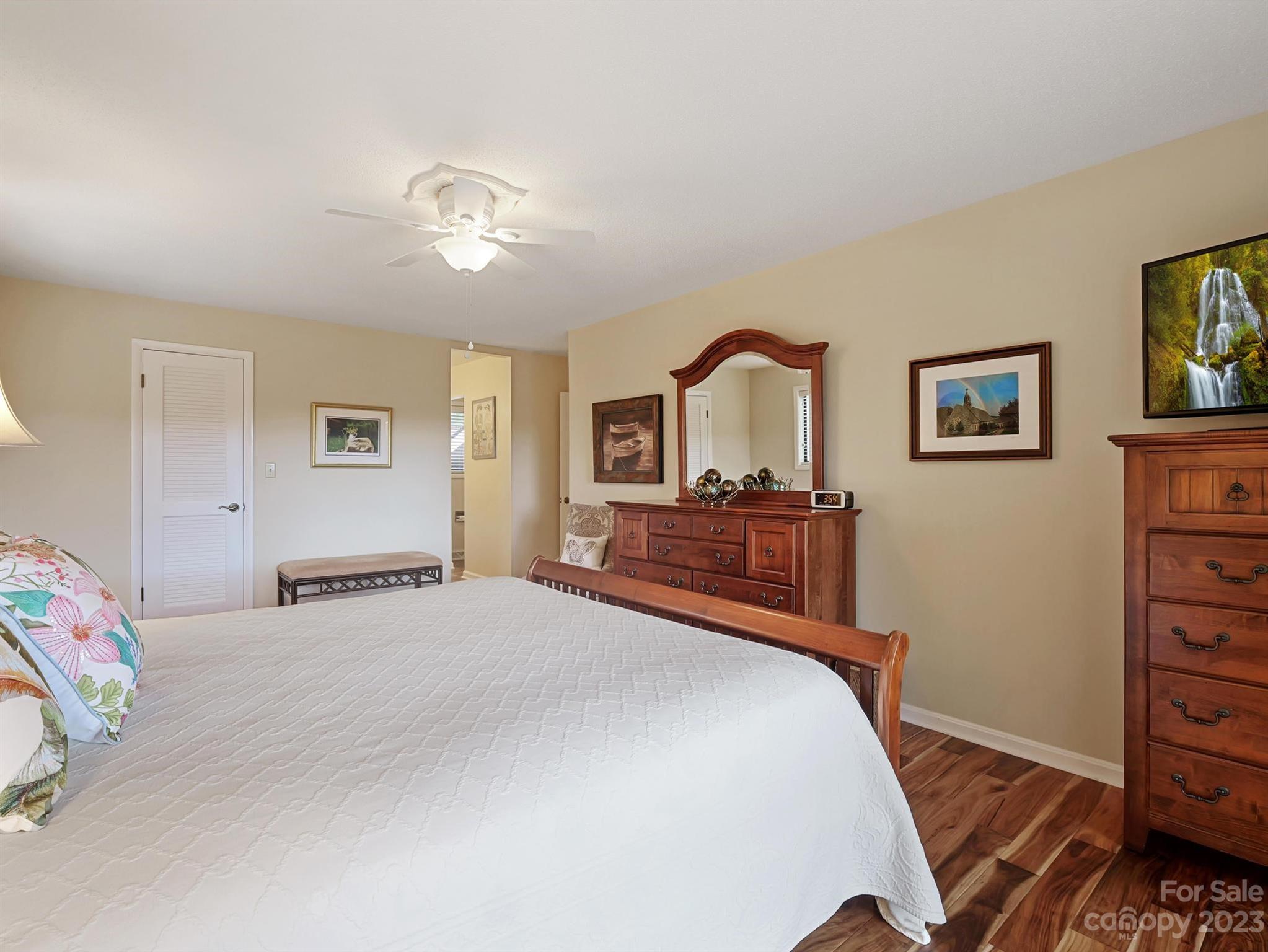 Furnished bedroom with a white quilted bed, wooden dressers, and warm wood-look flooring.