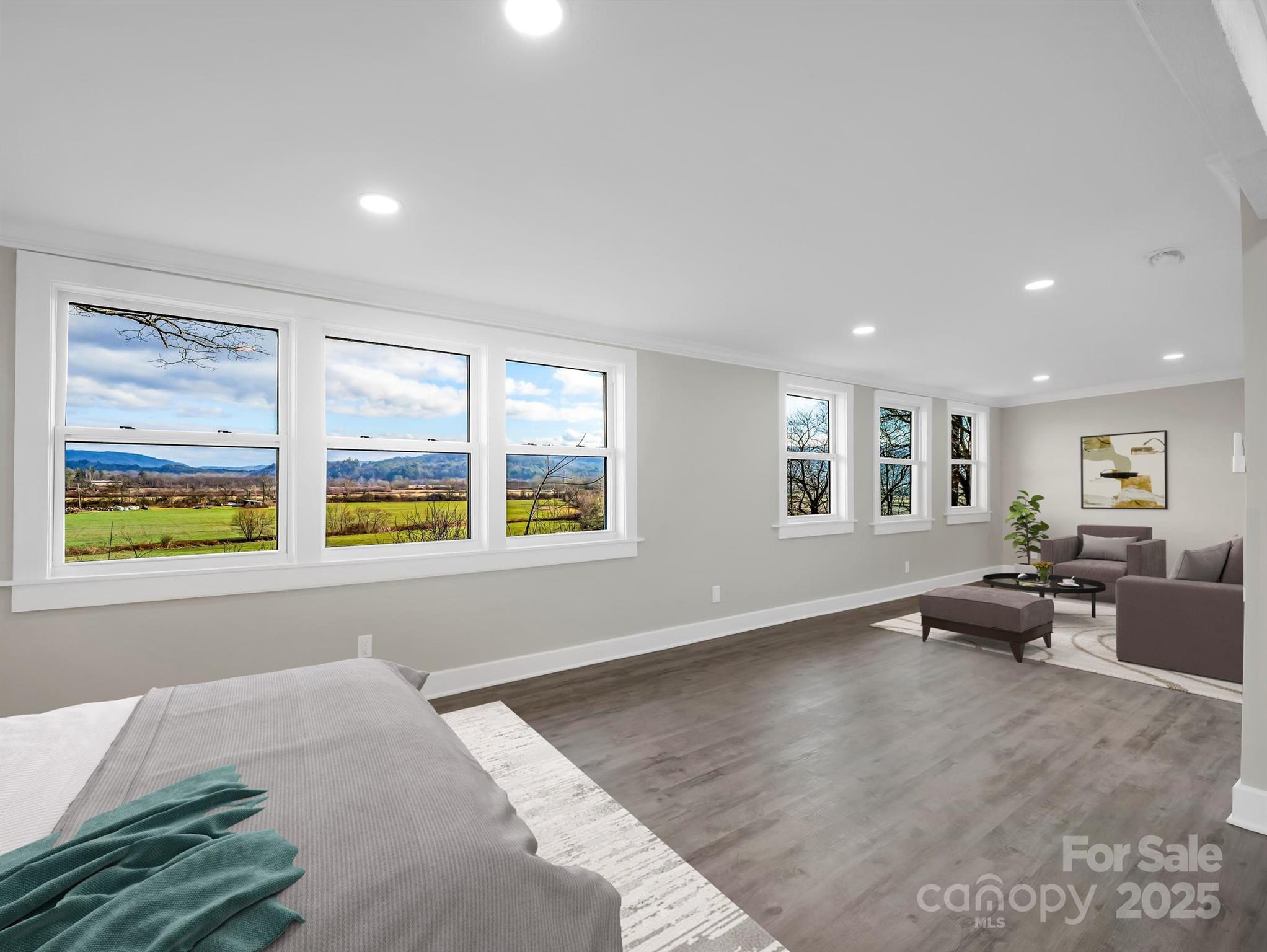 Bedroom and sitting area with large windows overlooking fields and distant mountains.