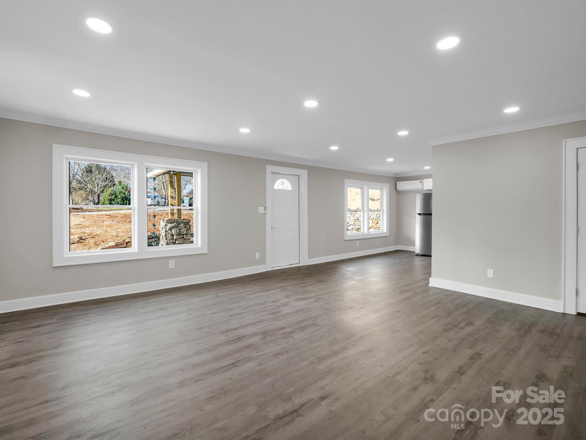 Empty room with gray wood-look floors, recessed lights, and large windows.