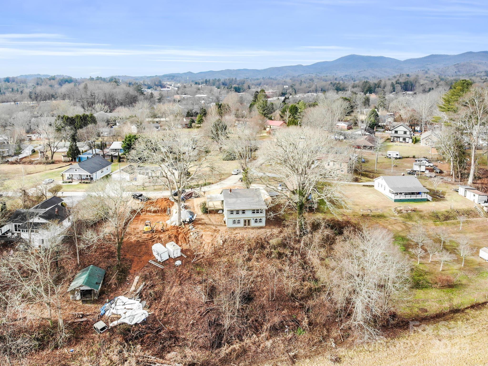 Aerial view of a two-story house on a wooded lot, with construction equipment and distant mountains.