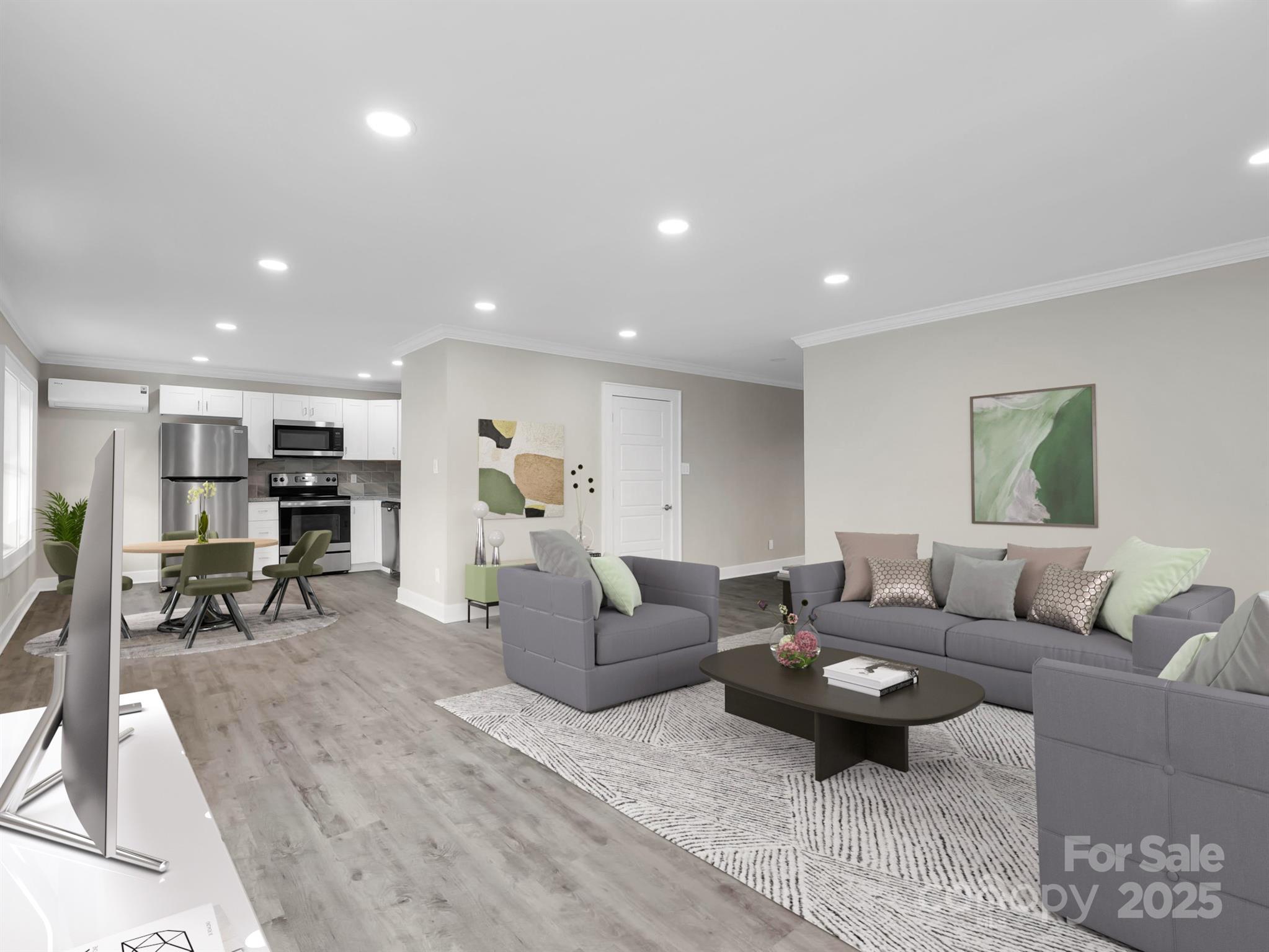 Open-plan living room with gray sofas and patterned rug beside a dining area and white kitchen.