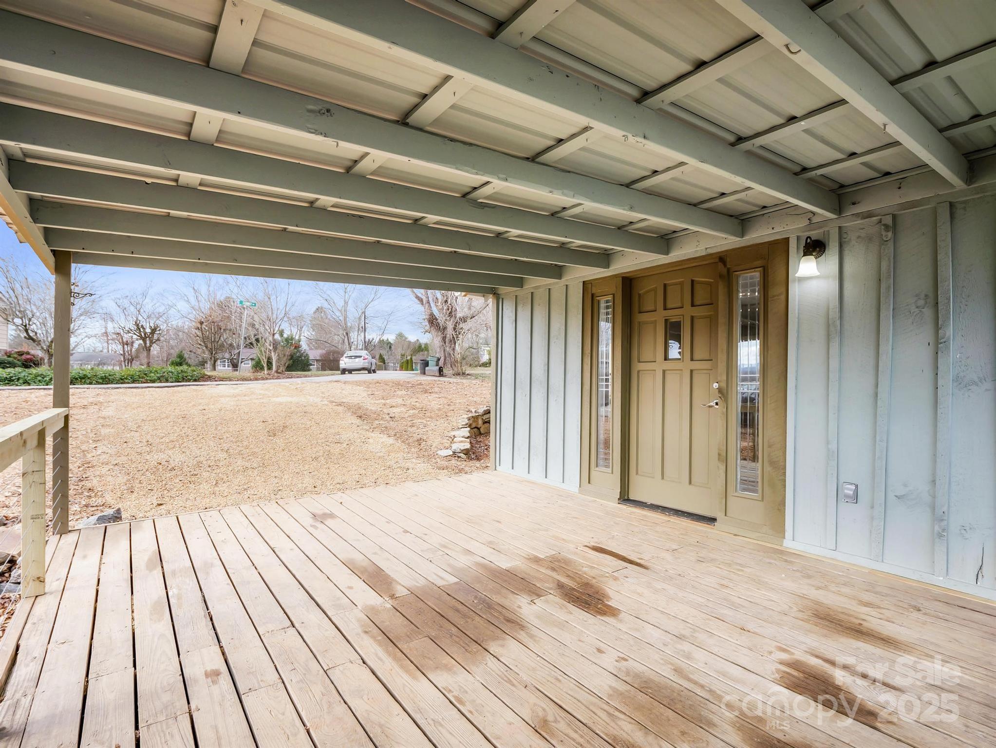 Covered wooden porch with a paneled front door overlooking a dormant yard.