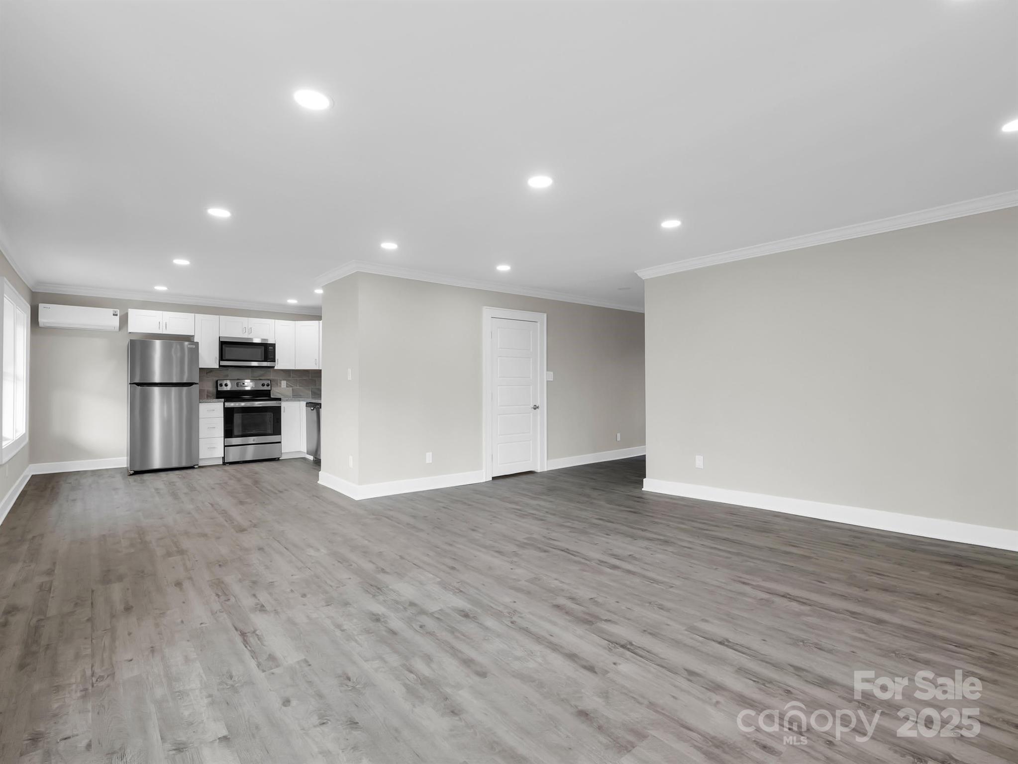 Vacant open-plan living area with gray plank flooring and a white-cabinet kitchen with stainless steel appliances.