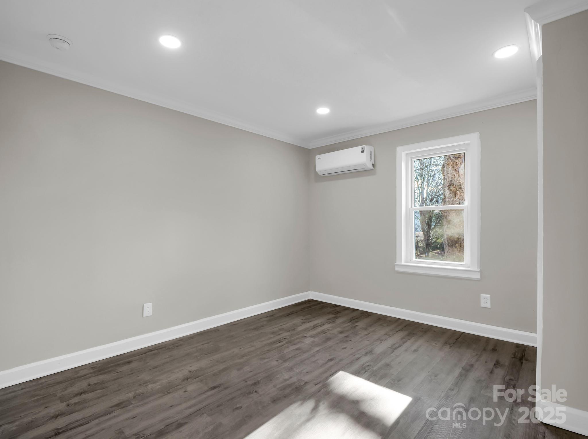 Vacant room with gray walls, dark wood-look flooring, a window, and a wall-mounted mini-split air conditioner.