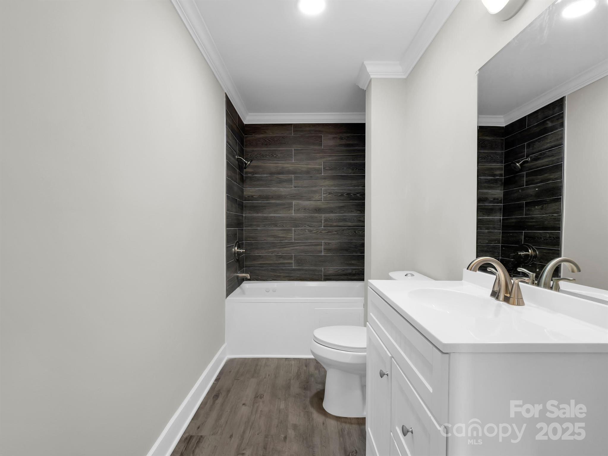 Bathroom with a dark tile tub surround, white vanity, and wood-look flooring.