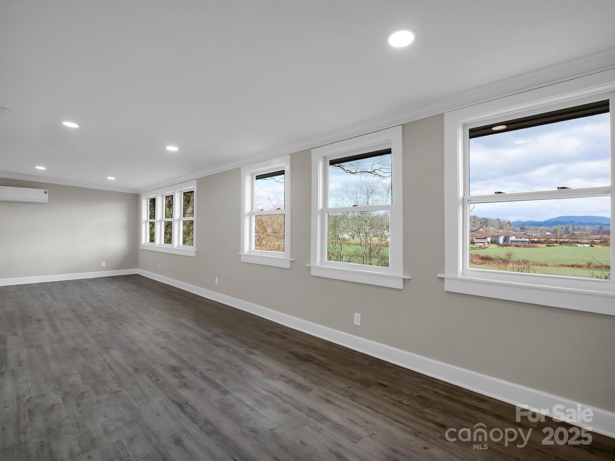 Empty room with large windows overlooking fields and distant mountains.