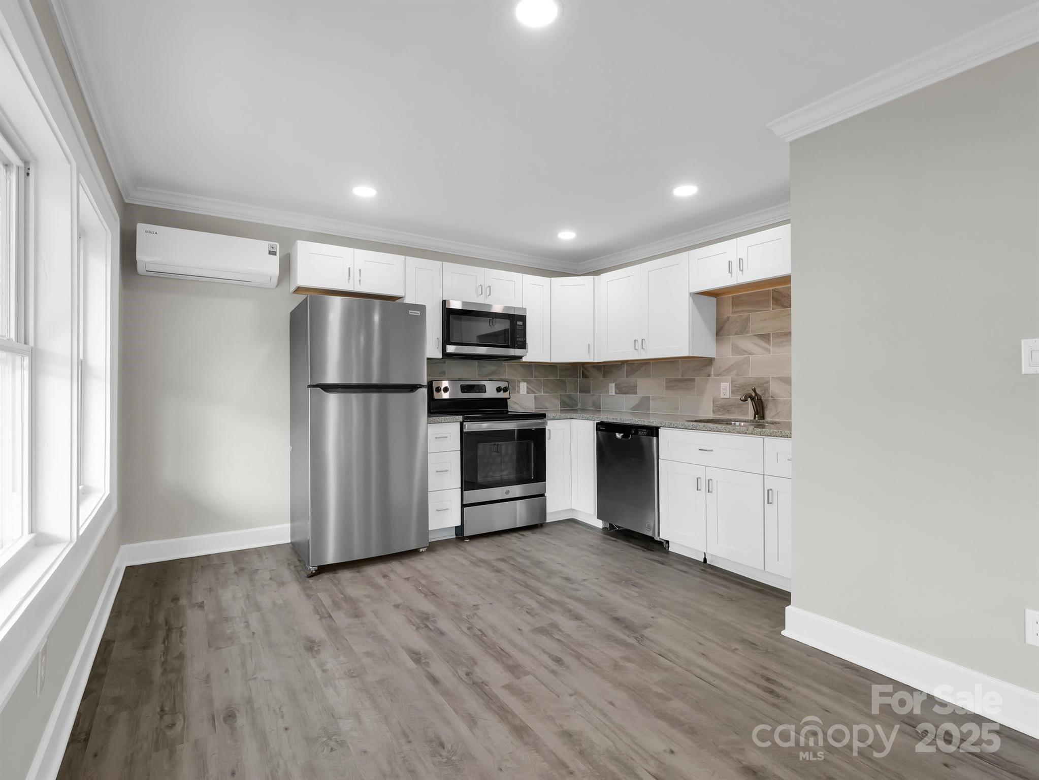 Vacant kitchen with white cabinets, stainless steel appliances, and a taupe tile backsplash.