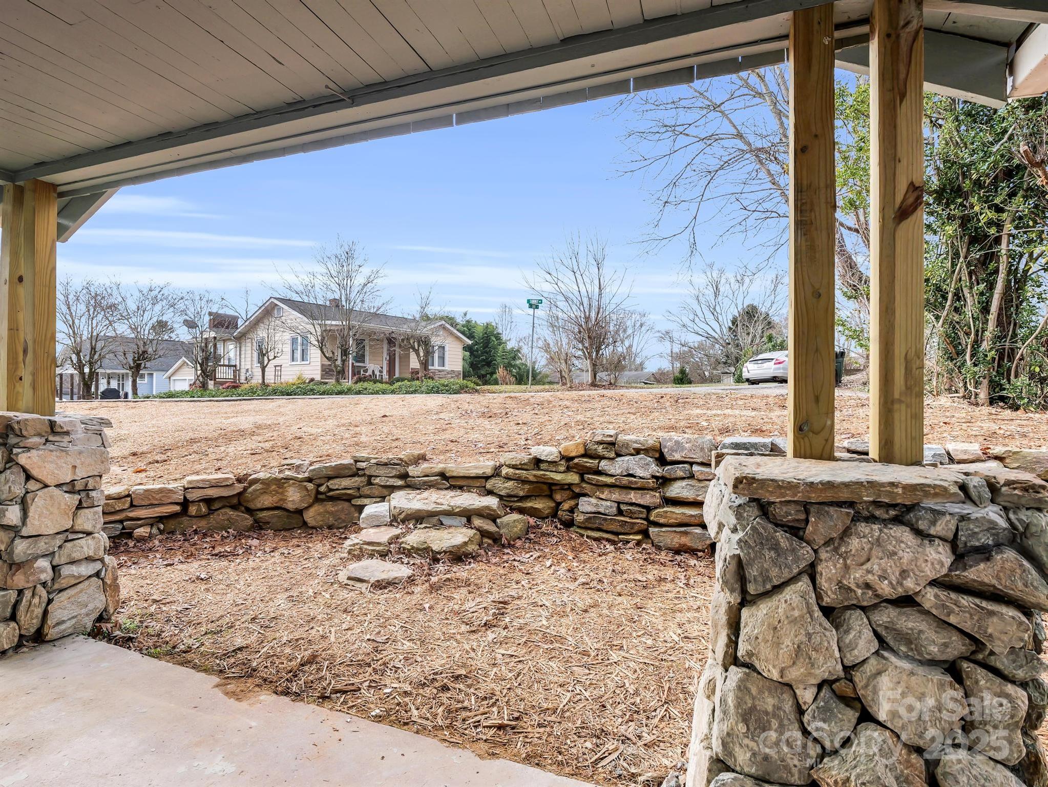 Covered porch overlooks a mulched yard with a stone retaining wall and neighboring homes.