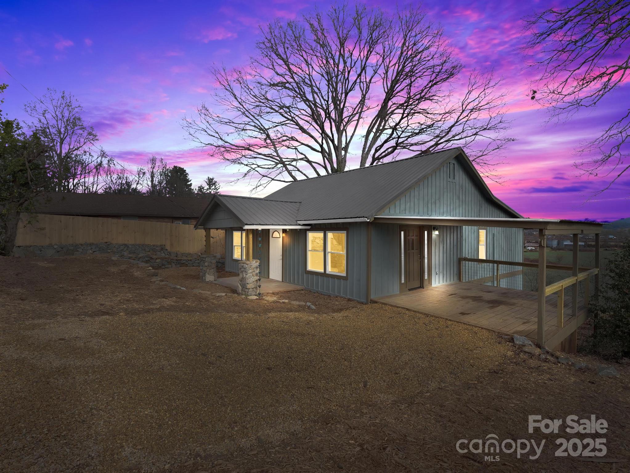 Gray-sided home with a metal roof and raised covered deck at sunset.