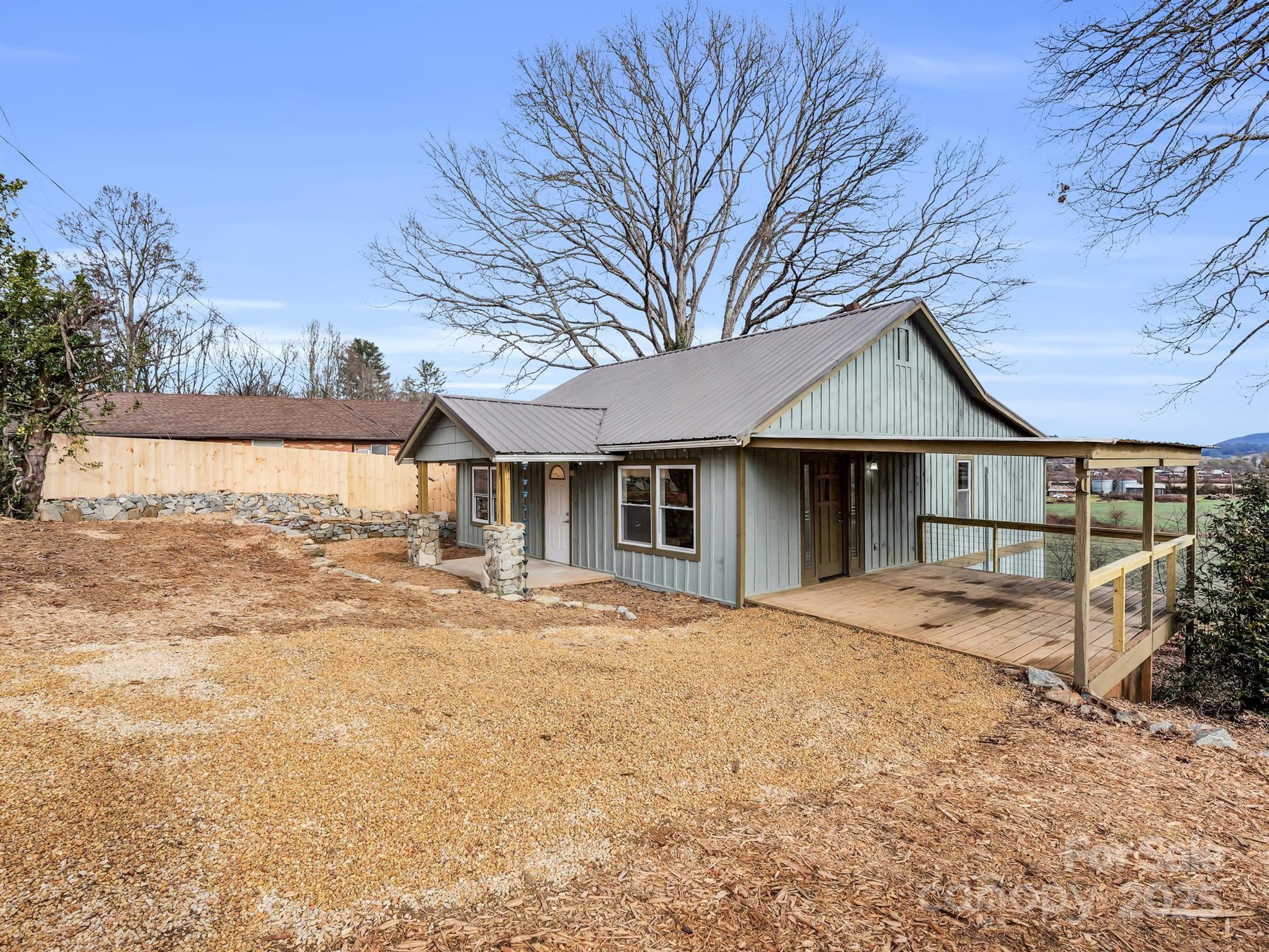 Gray-sided home with a metal roof and covered deck beside a gravel yard and leafless trees.