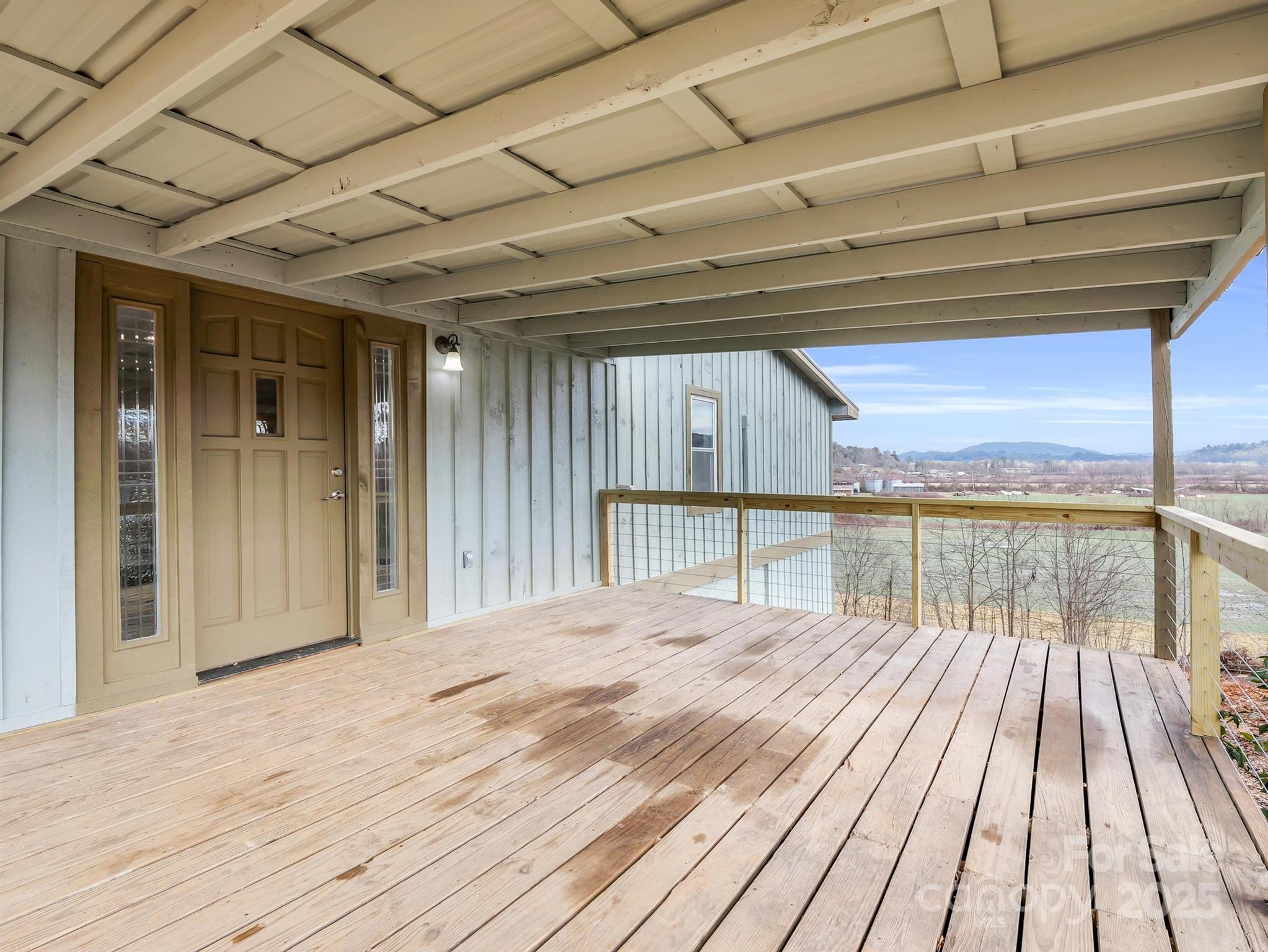 Covered wooden porch with cable railing and views of fields and distant mountains.