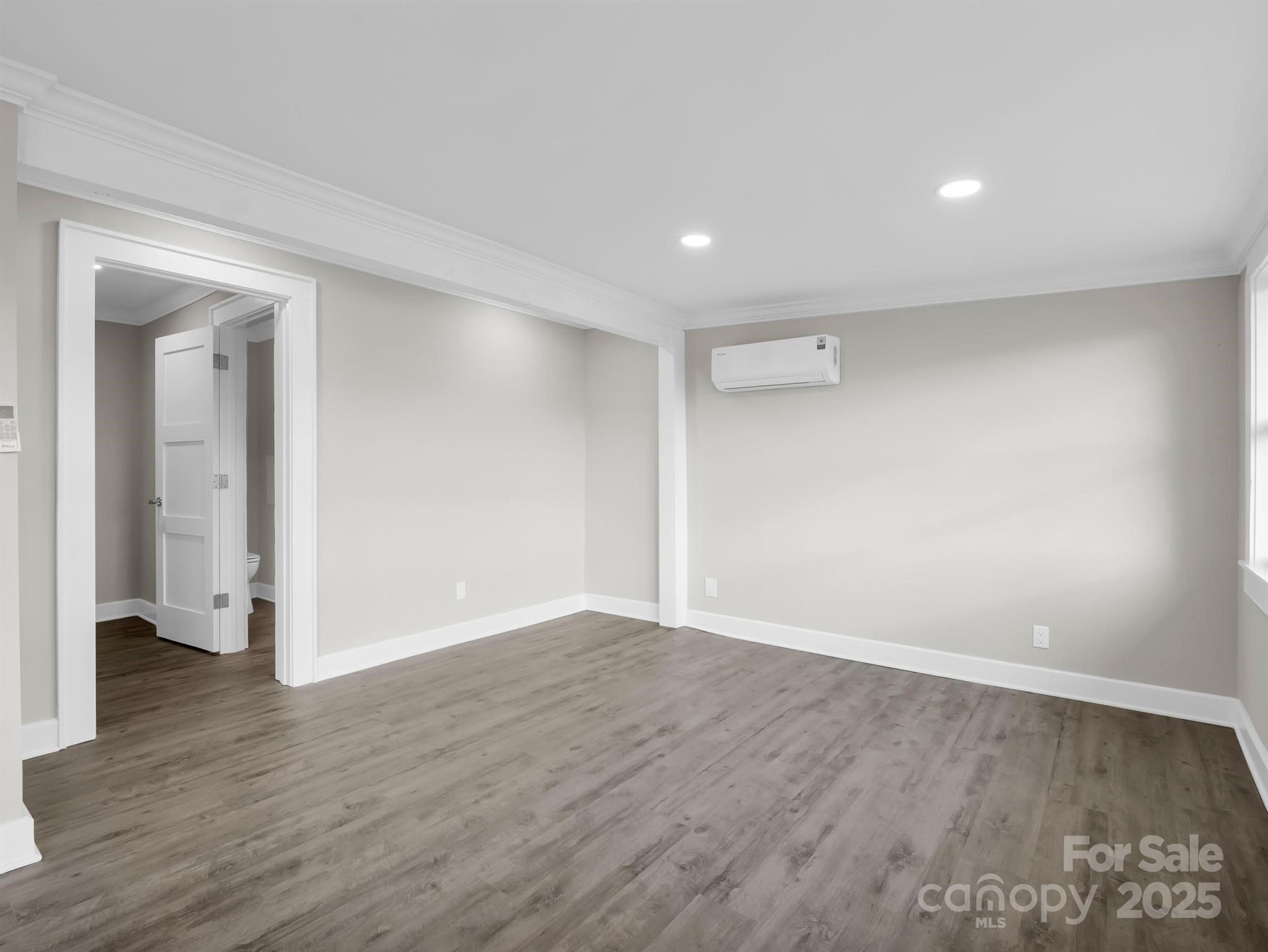 Empty room with gray wood-look flooring, recessed lights, and a wall-mounted mini-split air conditioner.