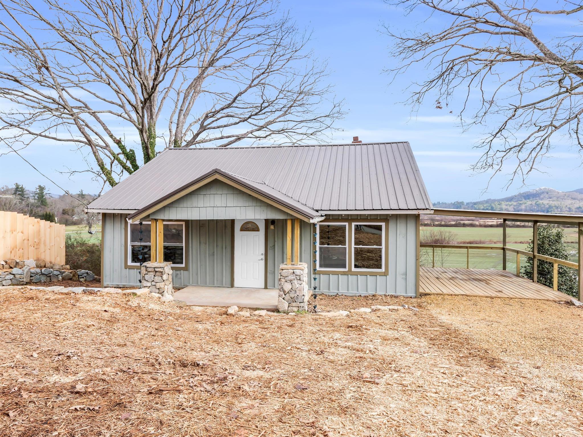 Gray cottage with a metal roof, stone porch columns, and a broad deck overlooking fields and hills.