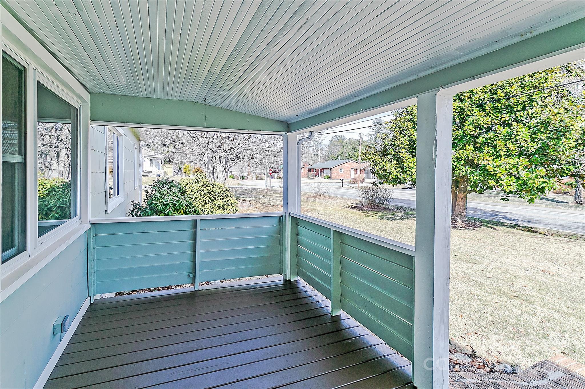 Covered porch with blue-green railings overlooking a lawn and residential street.