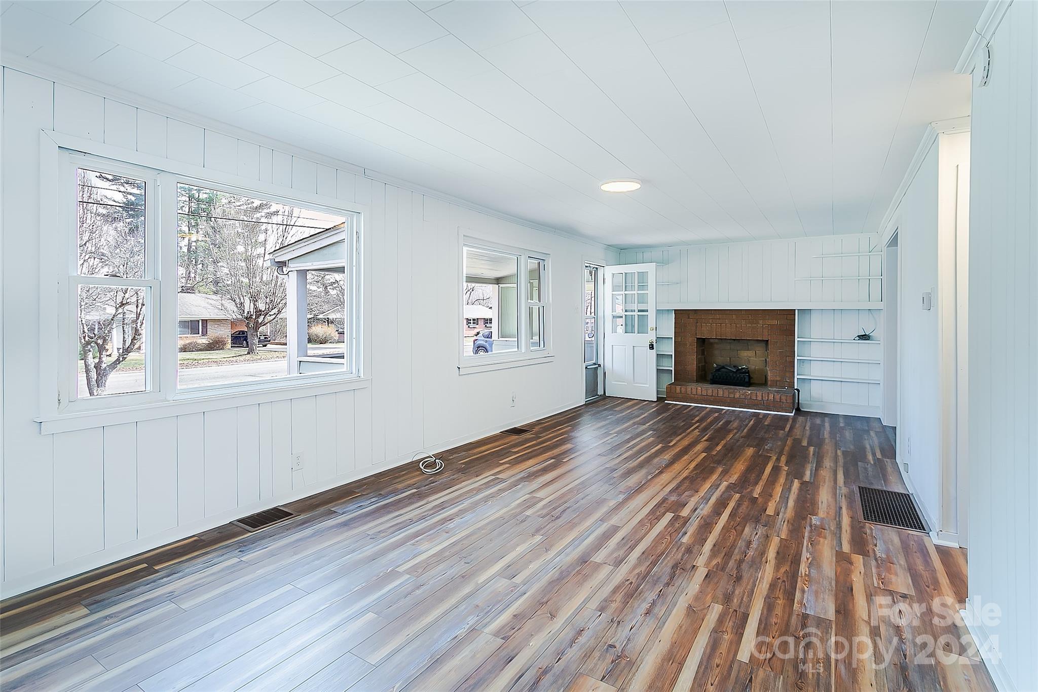 Vacant living room with a brick fireplace, built-in shelves, and mixed-tone wood flooring.