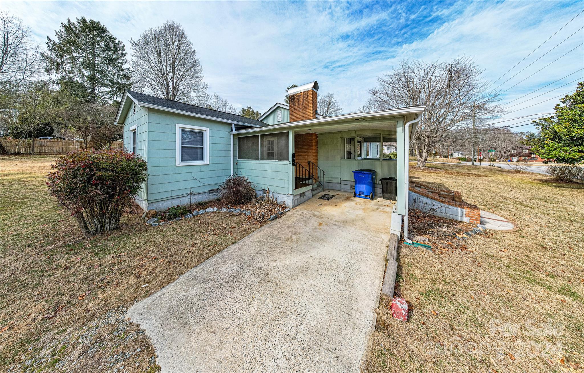 Light blue house with a covered carport, concrete driveway, and brick chimney.