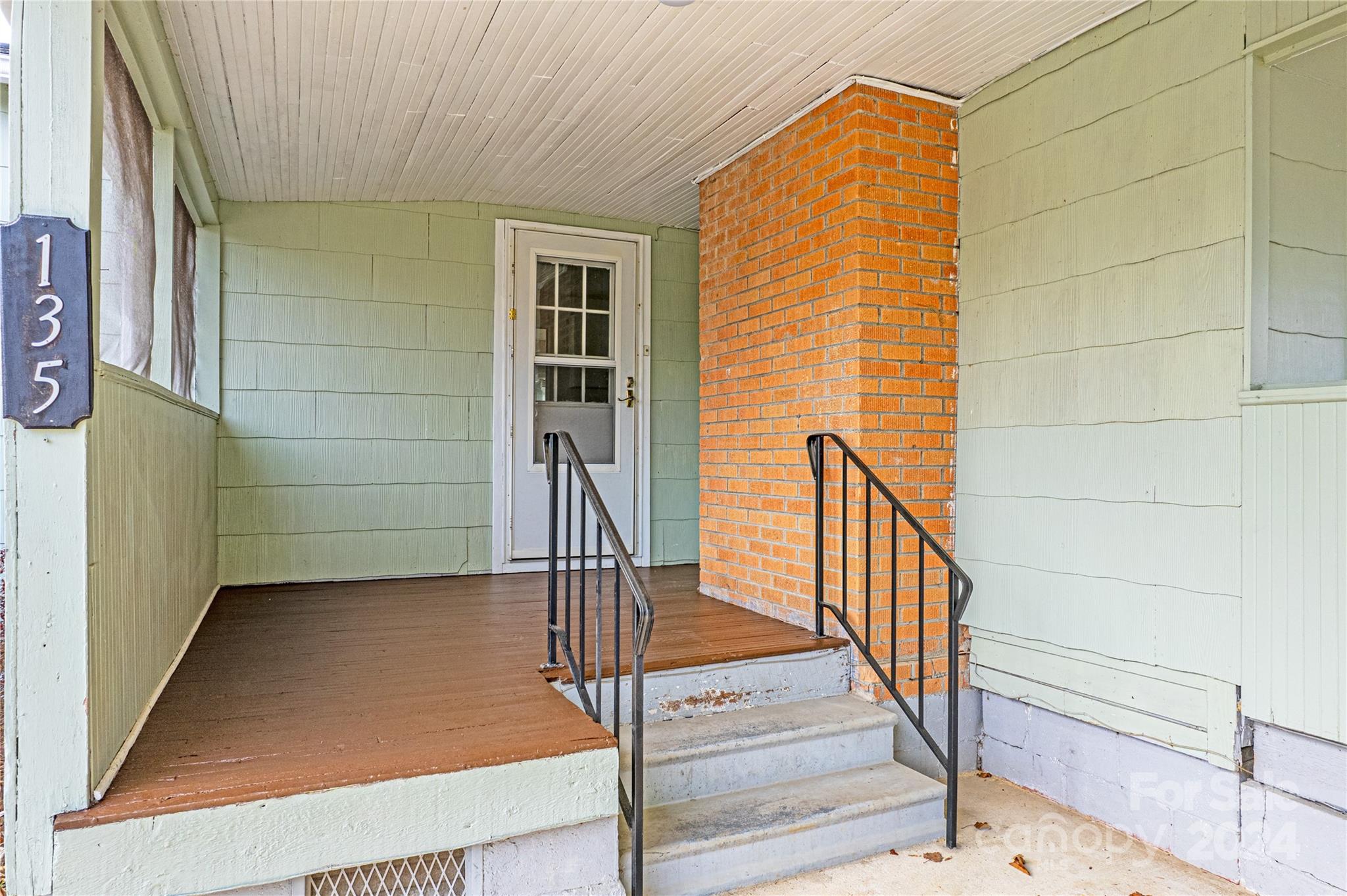 Covered porch entry with brick column, concrete steps, black railings, and a 135 address plaque.