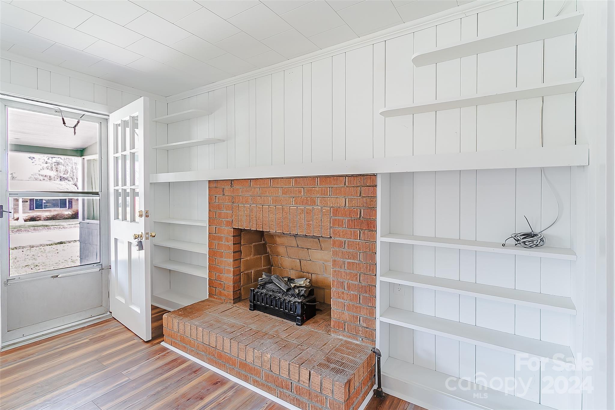 Brick fireplace with a raised hearth, surrounded by white built-in shelves and paneled walls.