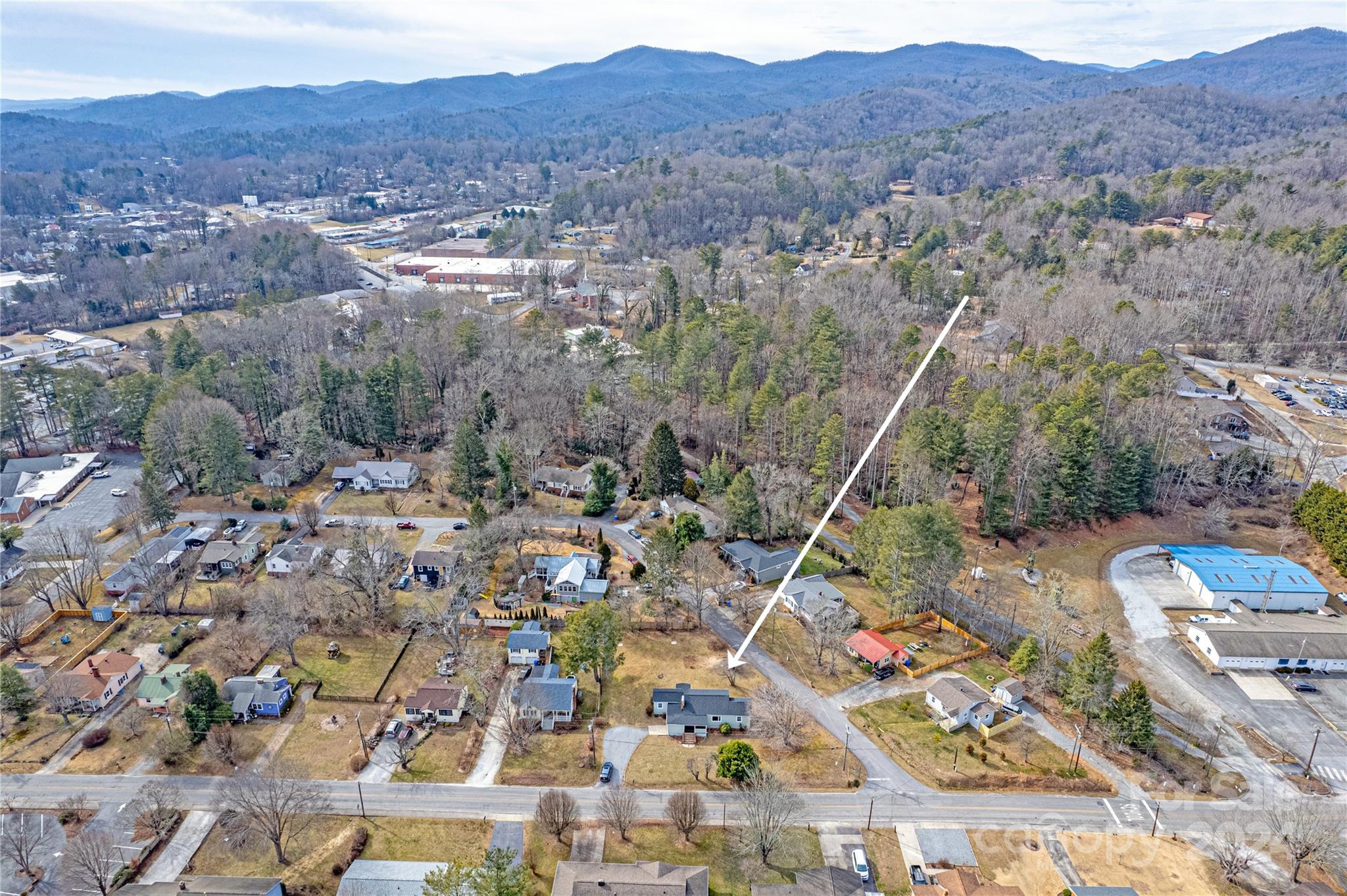 Aerial view of a residential lot marked by an arrow, with neighborhood homes and mountains beyond.