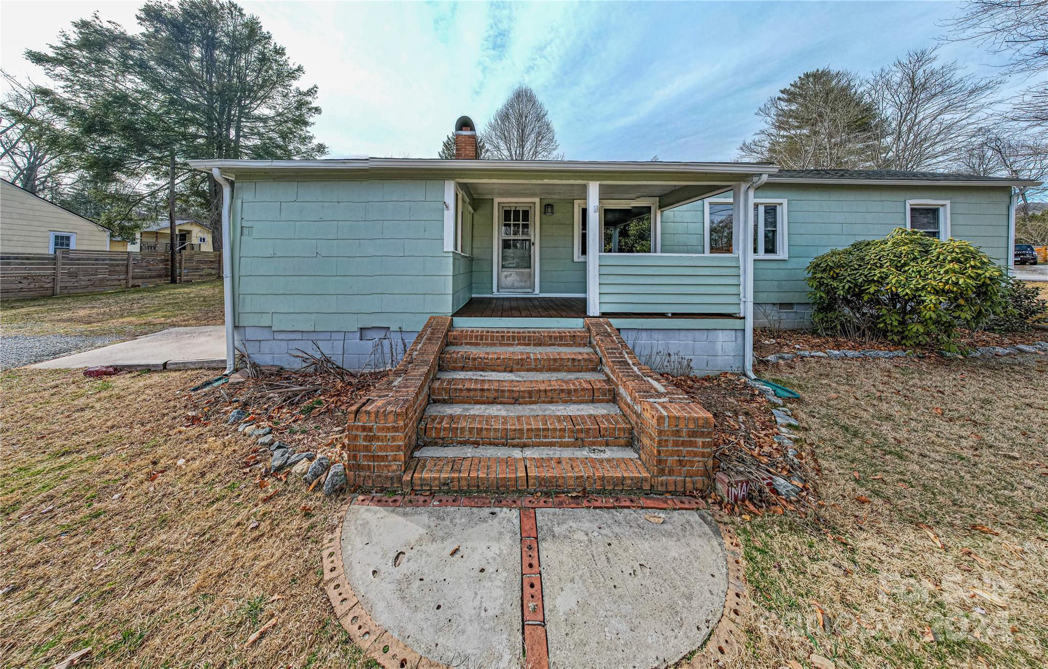 Blue-green single-story house with a covered porch and broad brick steps leading to a curved walkway.