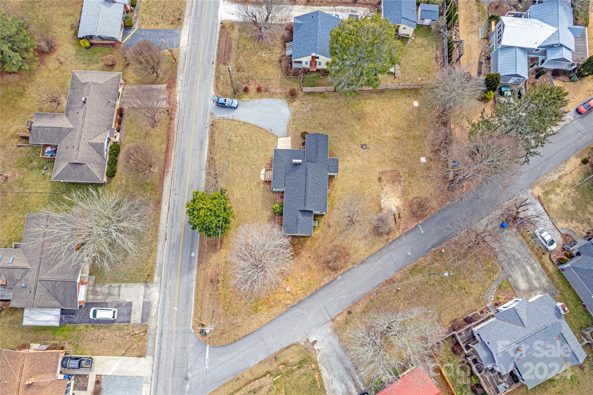 Aerial view of a house with a broad yard and gravel driveway beside a neighborhood road.