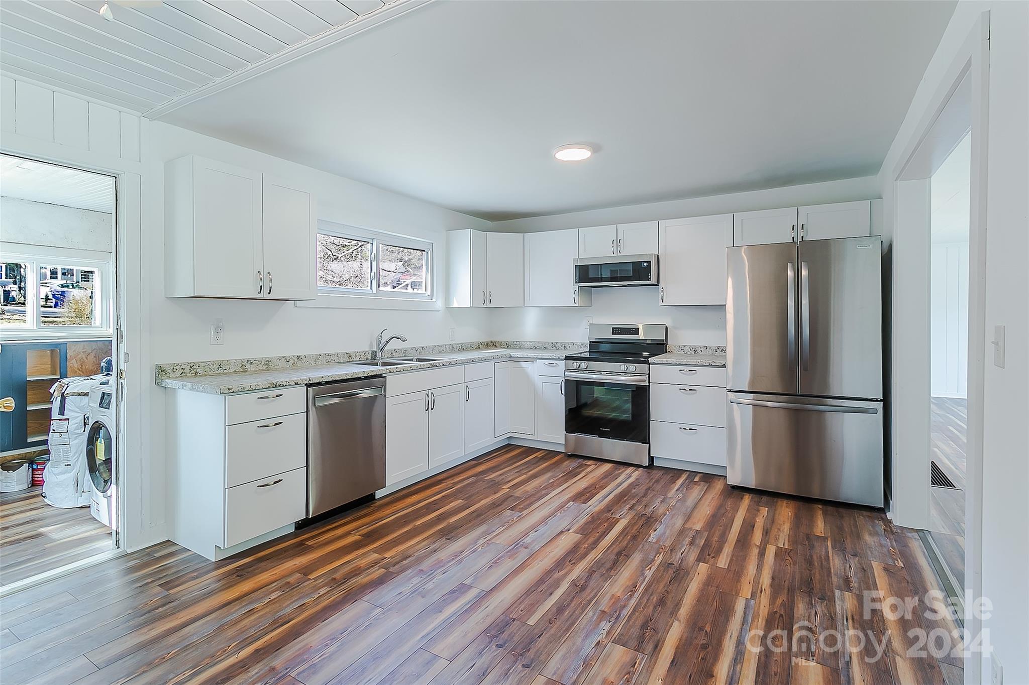 Unfurnished kitchen with white cabinets, stainless steel appliances, and wood-look flooring.