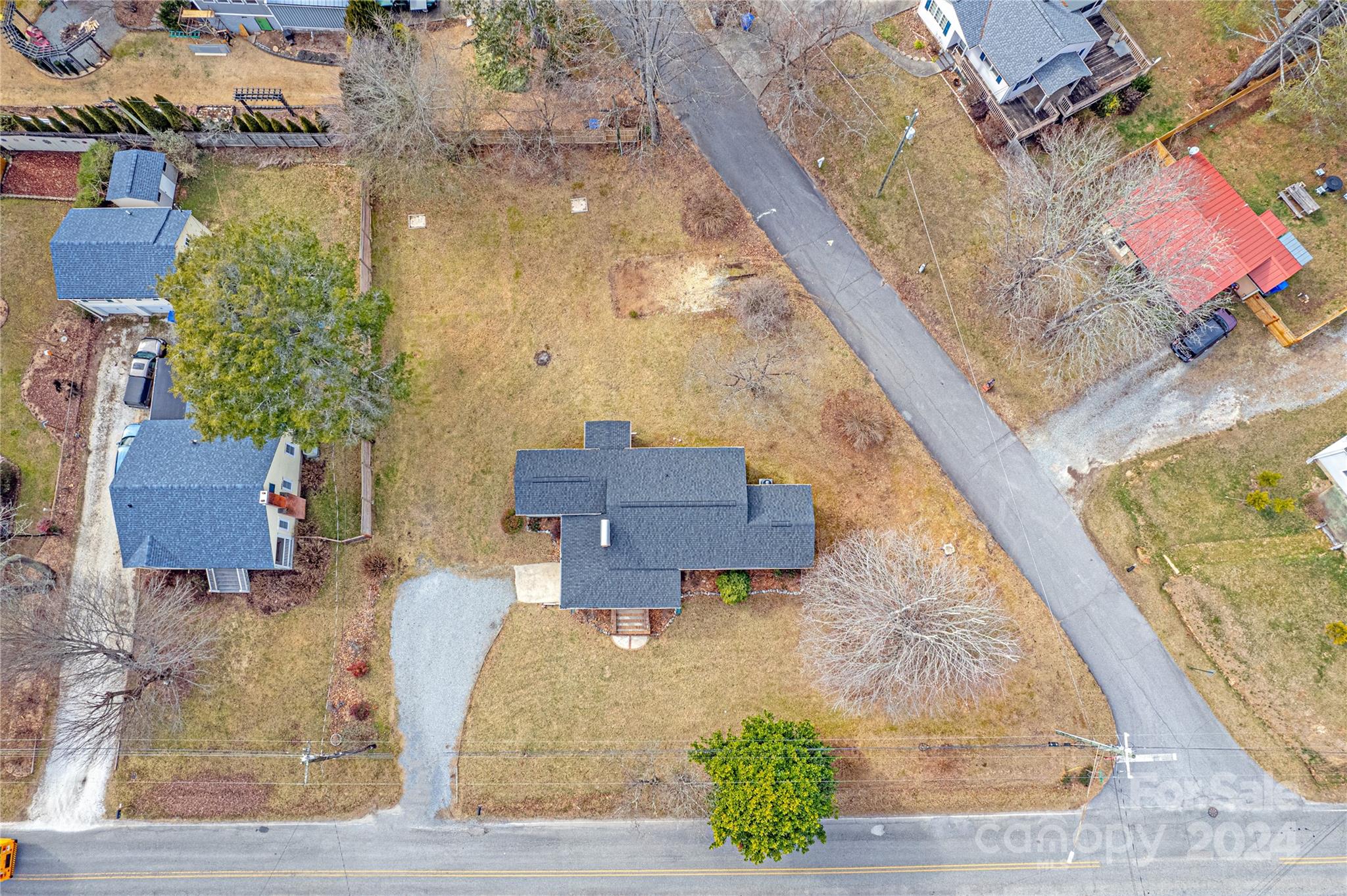 Aerial view of a gray-roofed house with a gravel driveway and broad lawn beside a residential road.