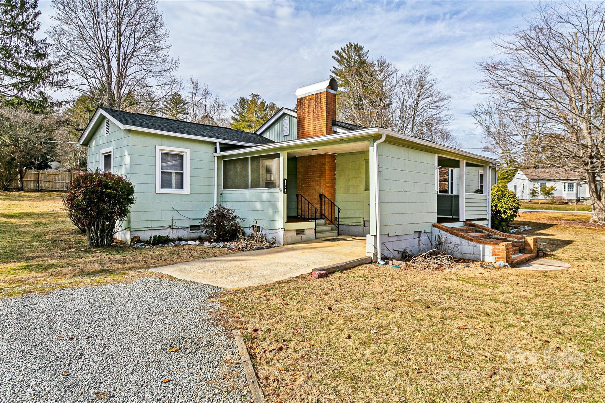 Light green single-story house with a covered entry, brick chimney, and gravel driveway.