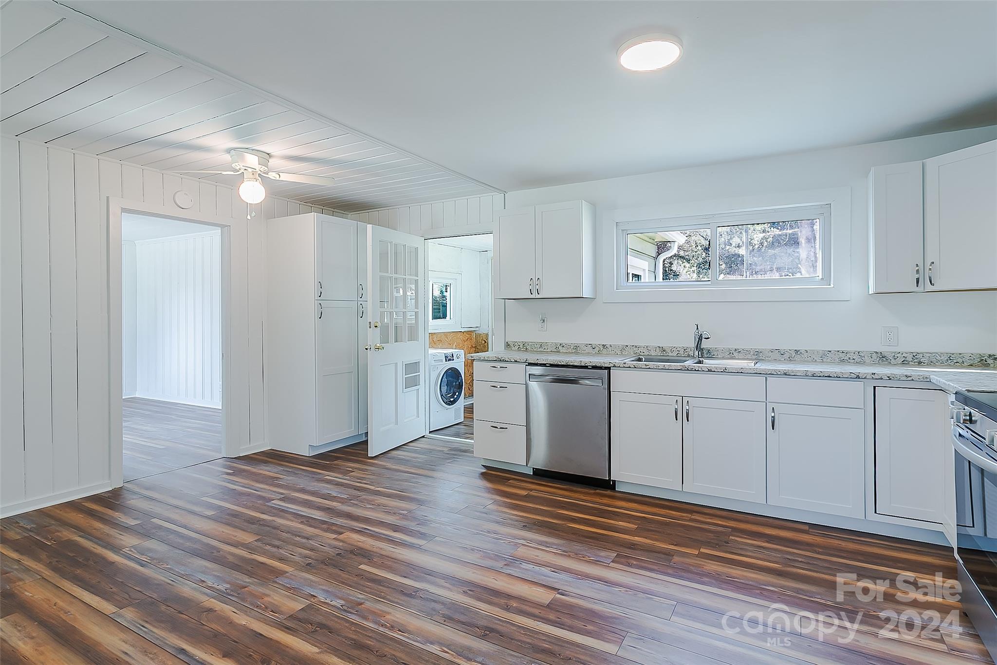 Kitchen with white cabinets, a stainless dishwasher, dark wood-look floors, and a washer visible through the doorway.