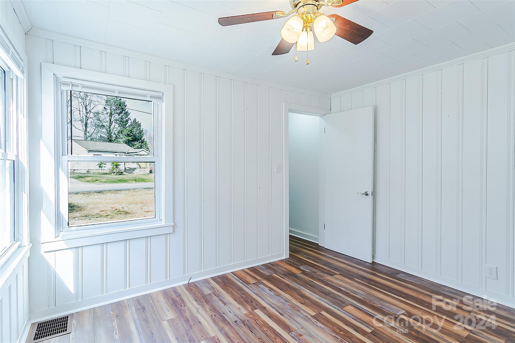 Empty room with white paneled walls, wood-look flooring, two windows, and a ceiling fan.