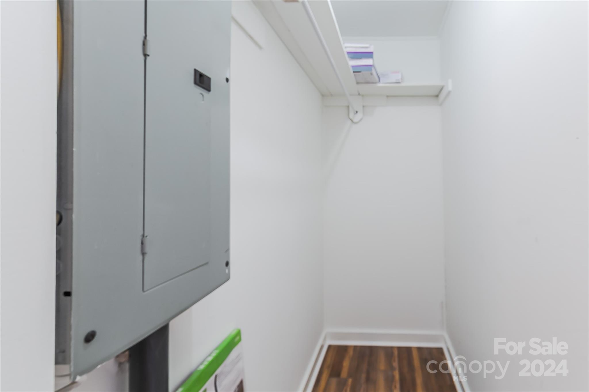 Utility closet with a large electrical panel, high shelf, and dark wood flooring.